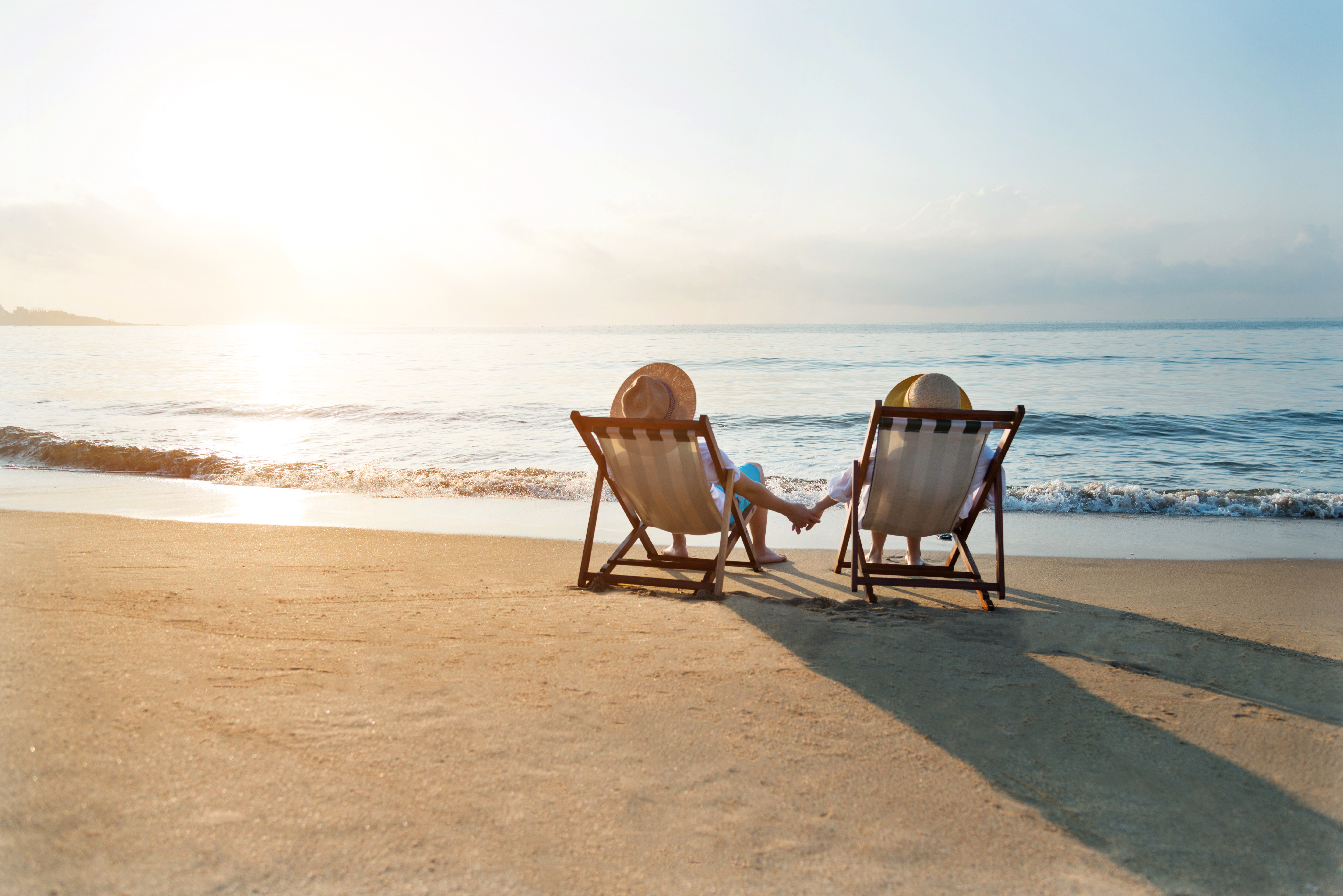 Couple sitting on deck chairs at beach during sunset, watching waves roll in