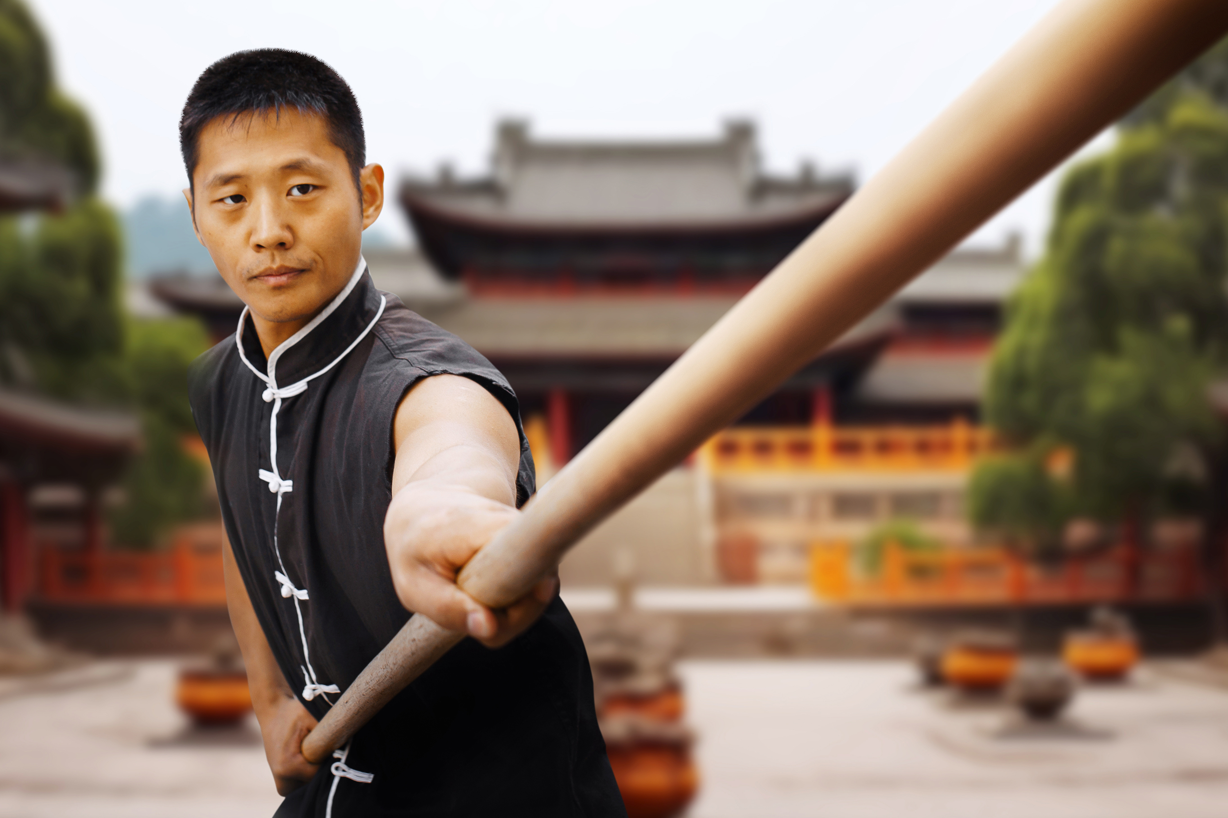 a man practicing with a martial arts staff in front of a temple