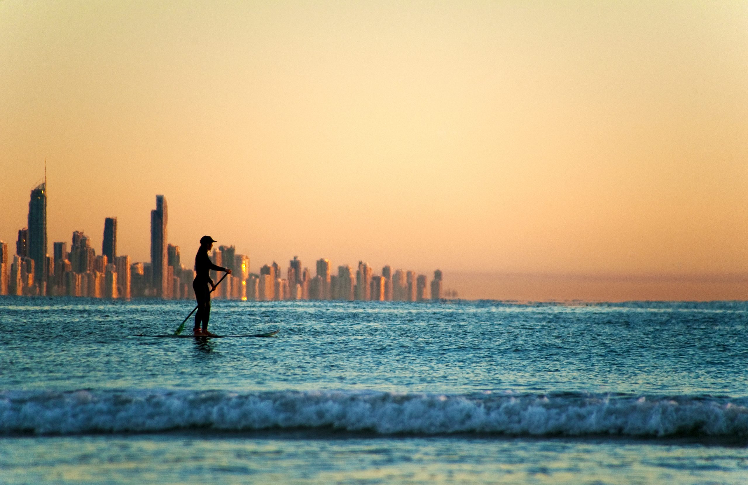 person on paddleboard off coast with city in background