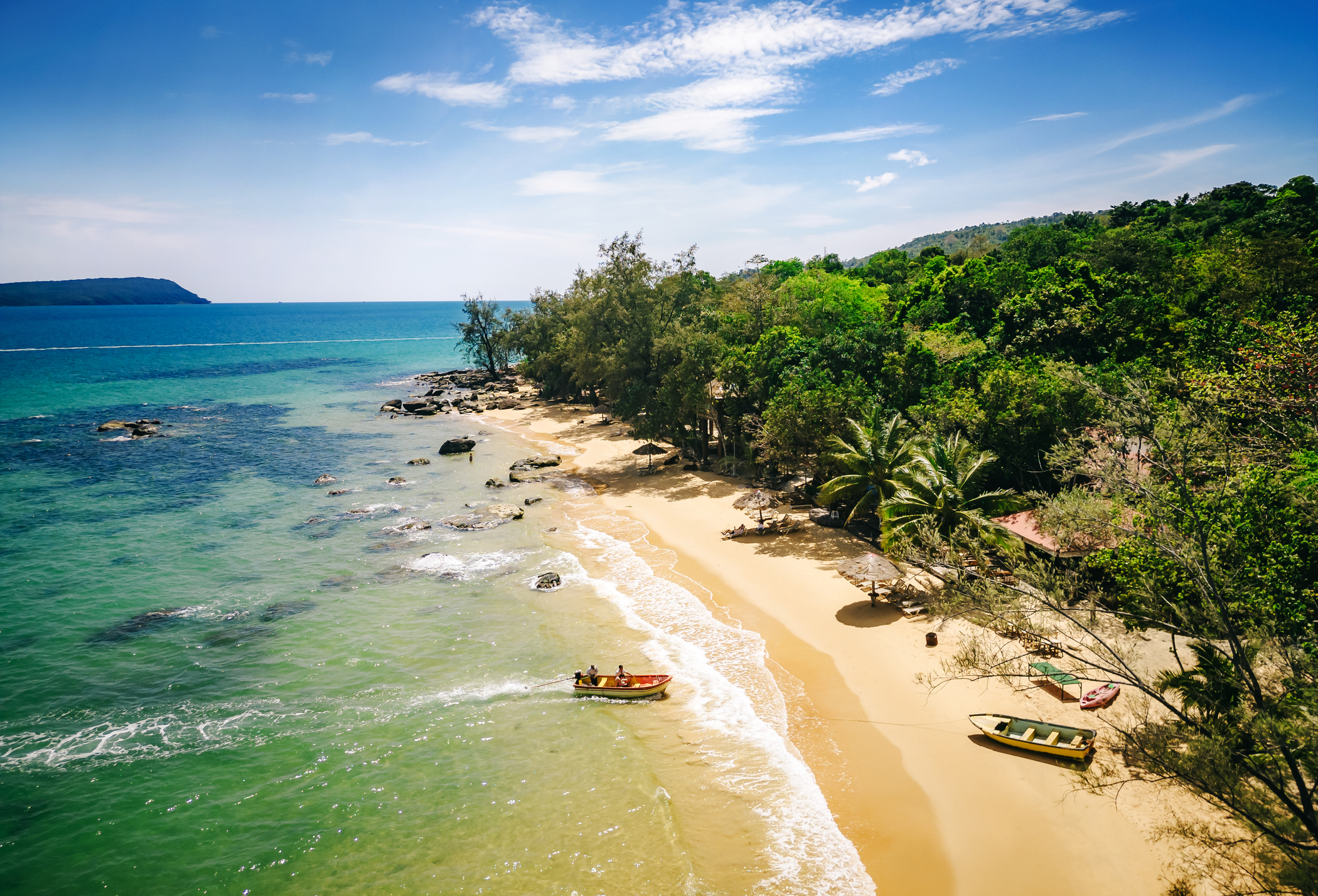 An aerial view of a pristine sandy beach and jungle with some boats coming in on Koh Rong island in Cambodia.
