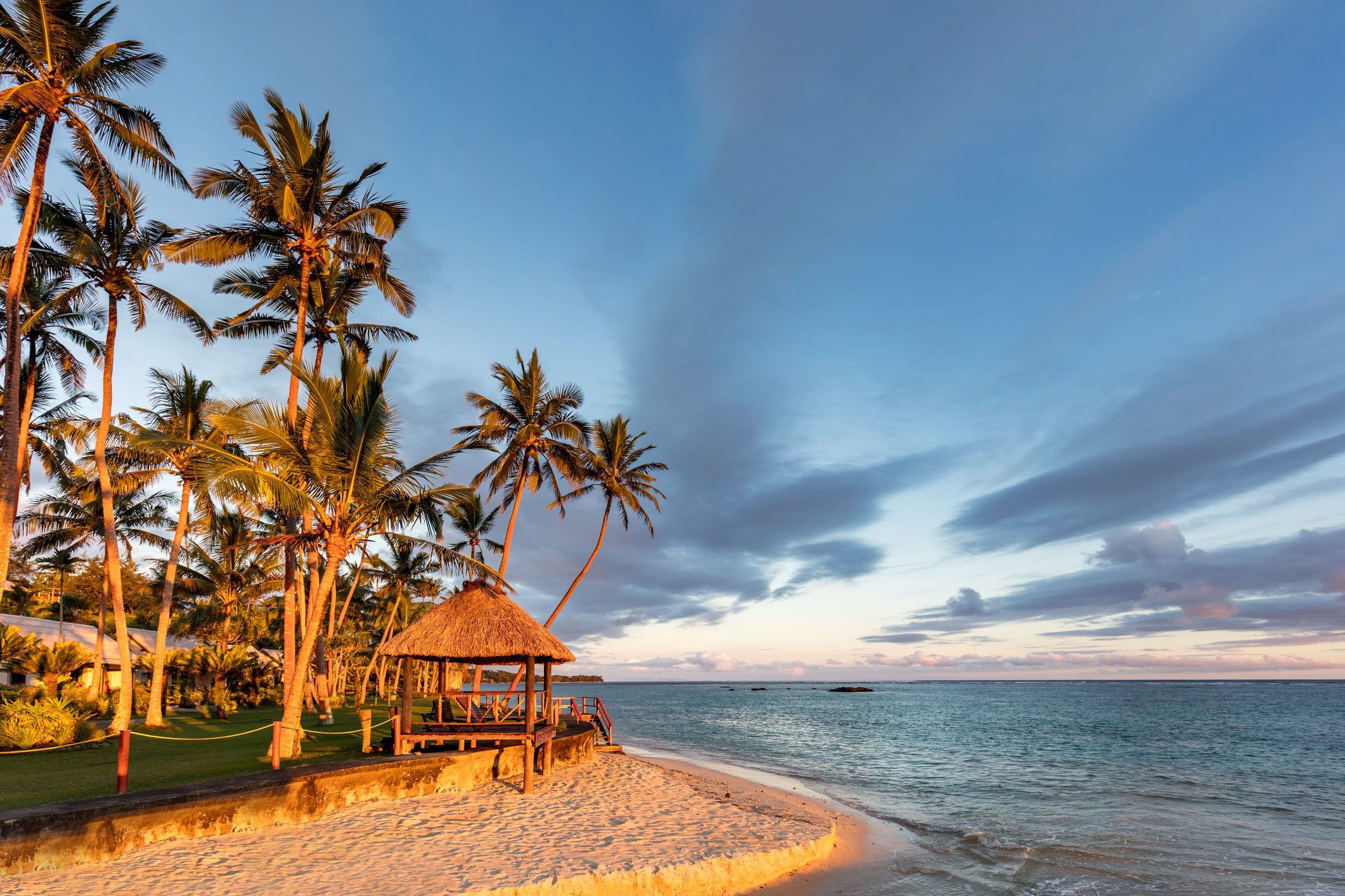 A beach on Fiji's Coral Coast at sunset, with the palm trees swaying and the ocean breeze sweeping through the island.