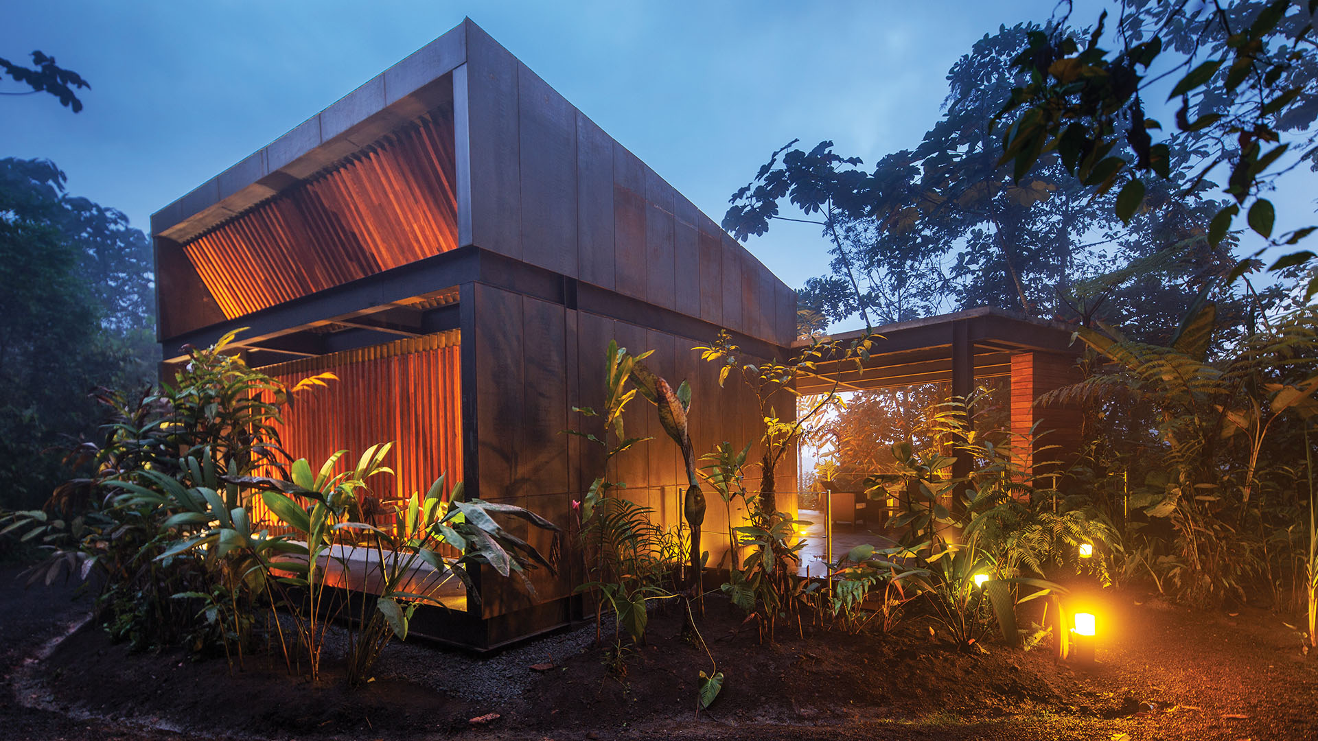 The modern cube shaped Mashpi Lodge at dusk, illuminated by warm orange lights