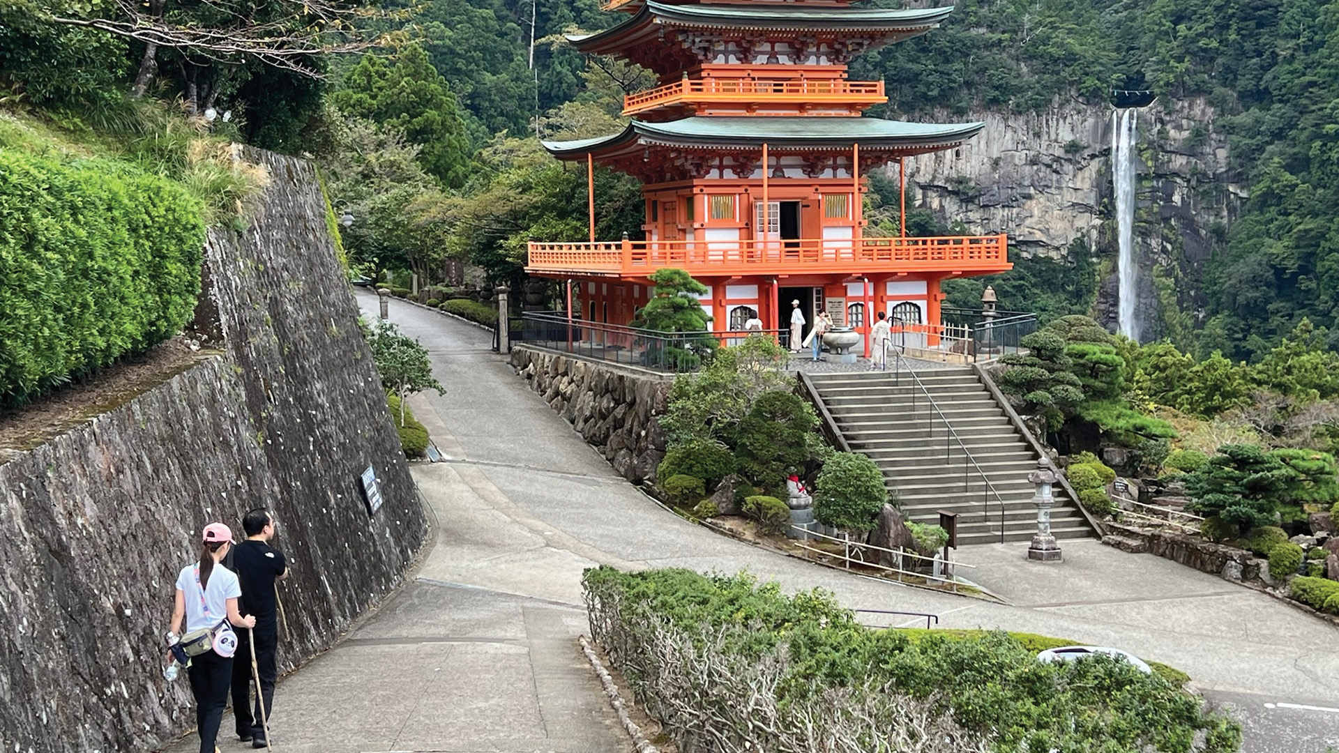 hikers on a trail leading to a Japanese temple and waterfall