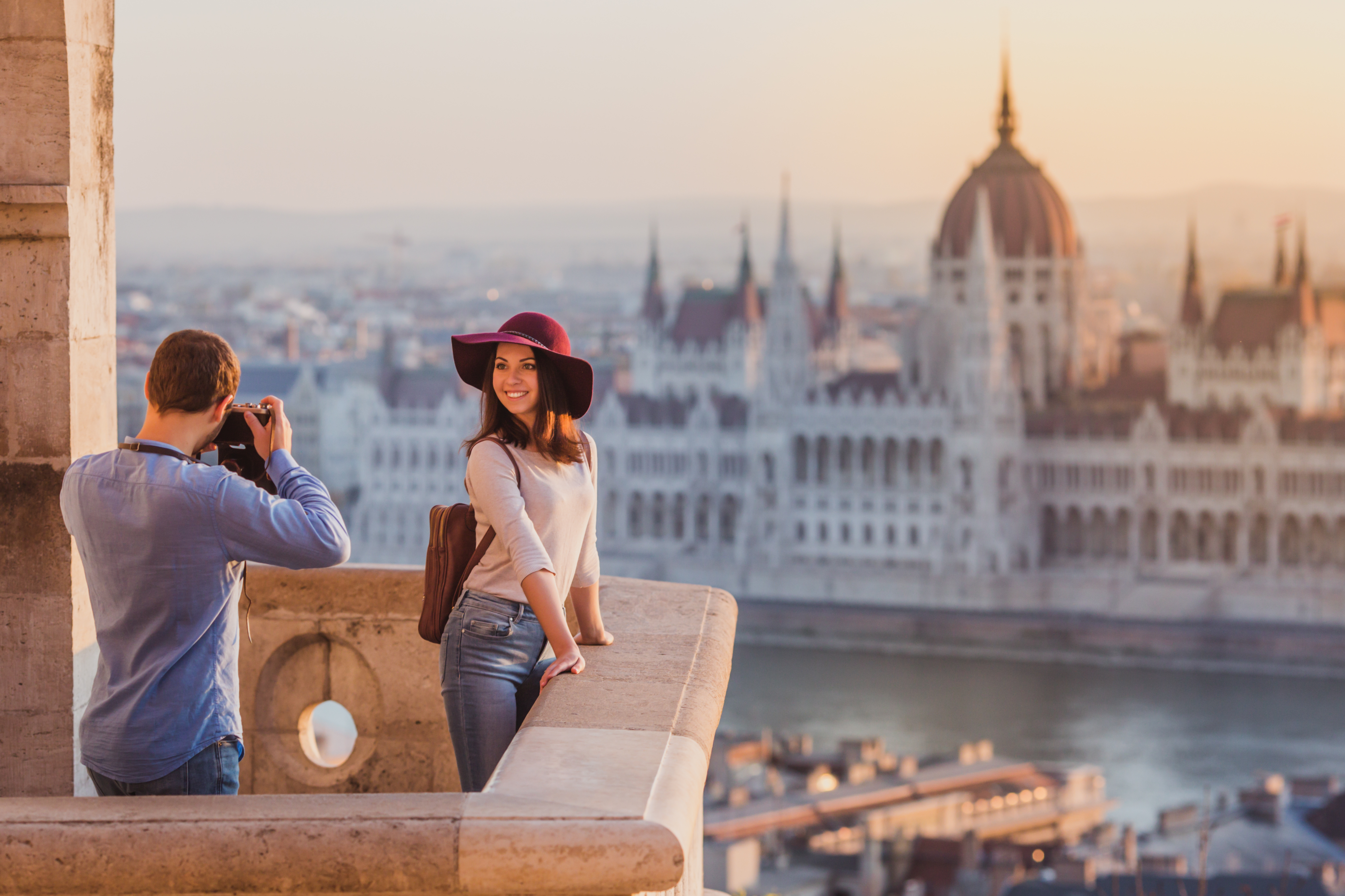 man taking photo of woman overlooking river with city backdrop