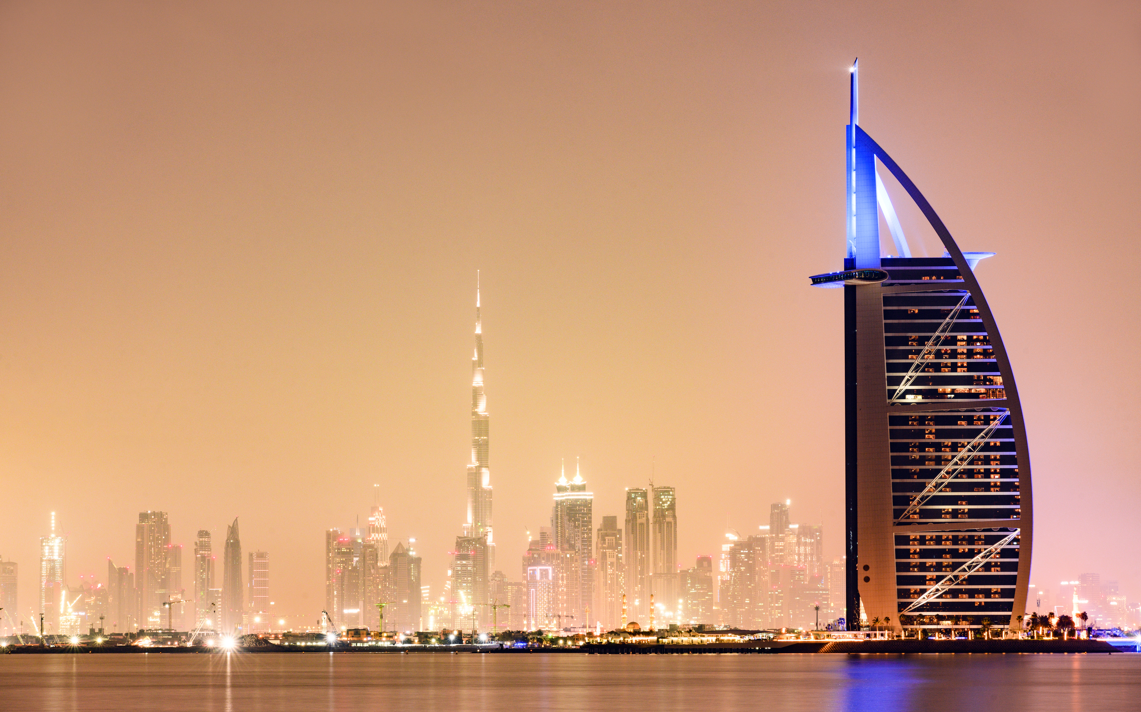 Stunning view of the illuminated Dubai skyline during sunset with the magnificent Burj Khalifa in the background and the seven stars luxury hotel Burj Al Arab in the foreground. Dubai, United Arab Emirates