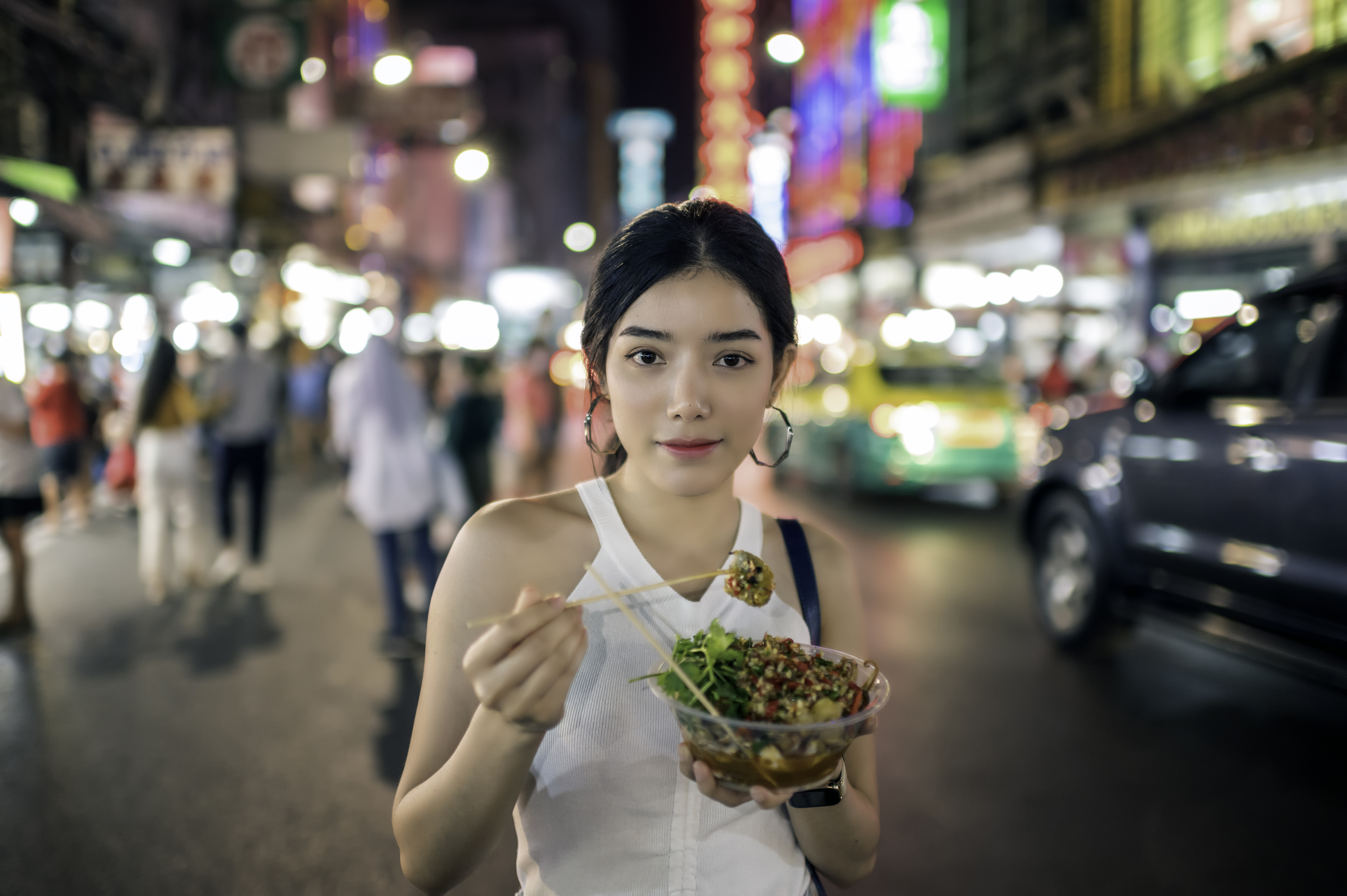 young woman eating grilled squid in Chinatown, Bangkok, Thailand.