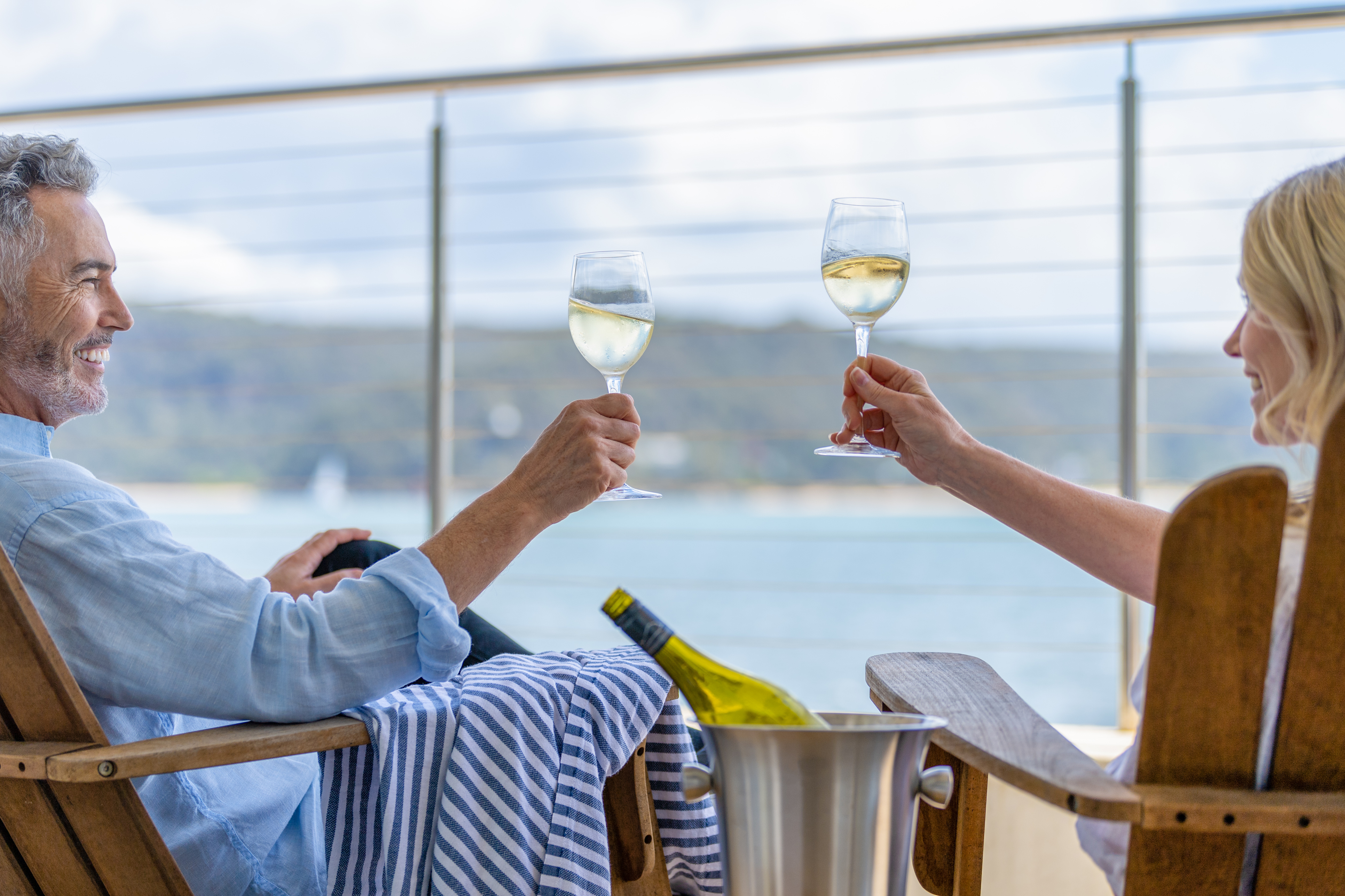 Mature couple drinking wine out on the deck. They are happy and smiling sitting in deck chairs.