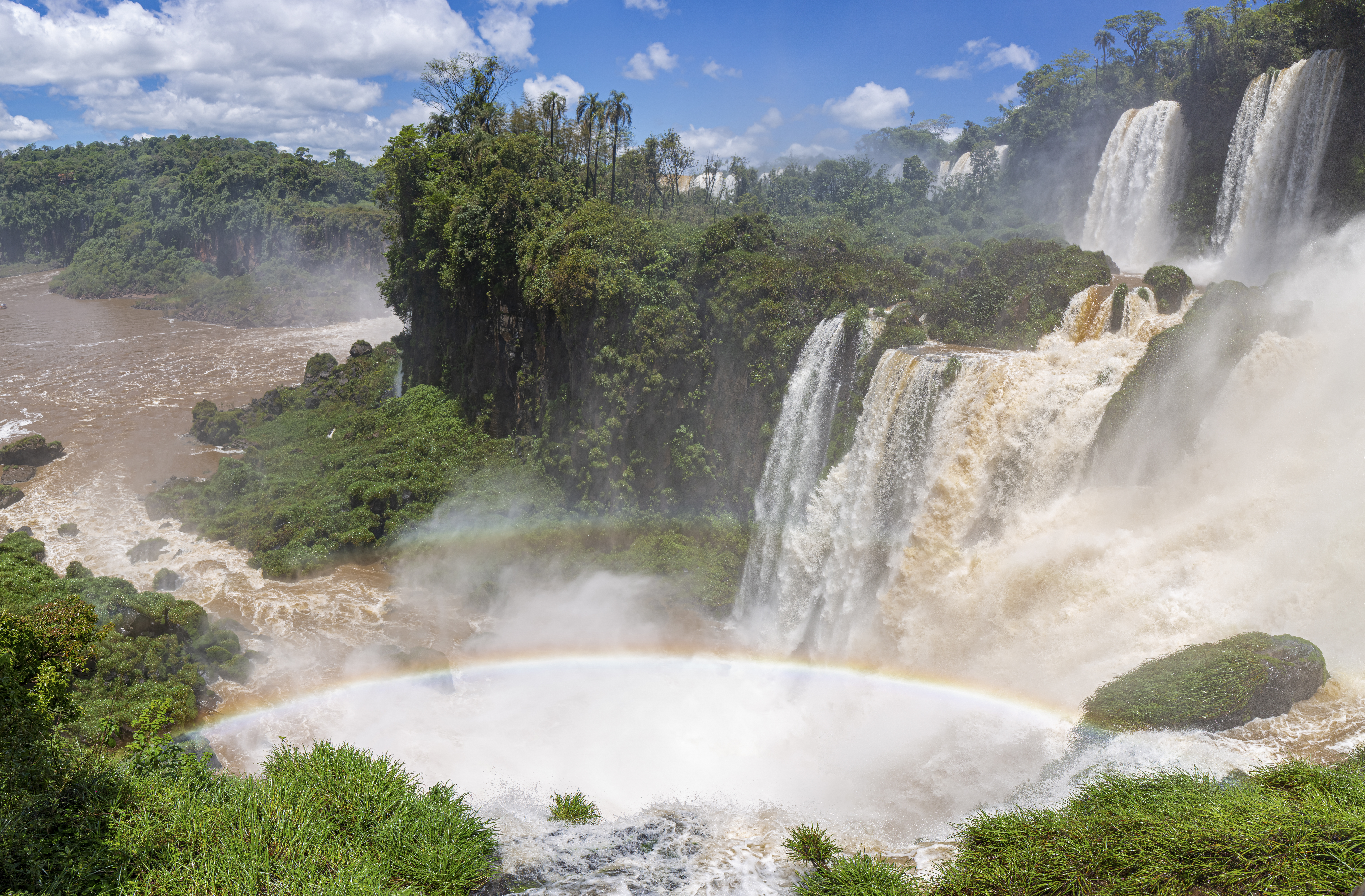 Impressive Iguazu Falls with rainbow and blue sky with white clouds, Argentina