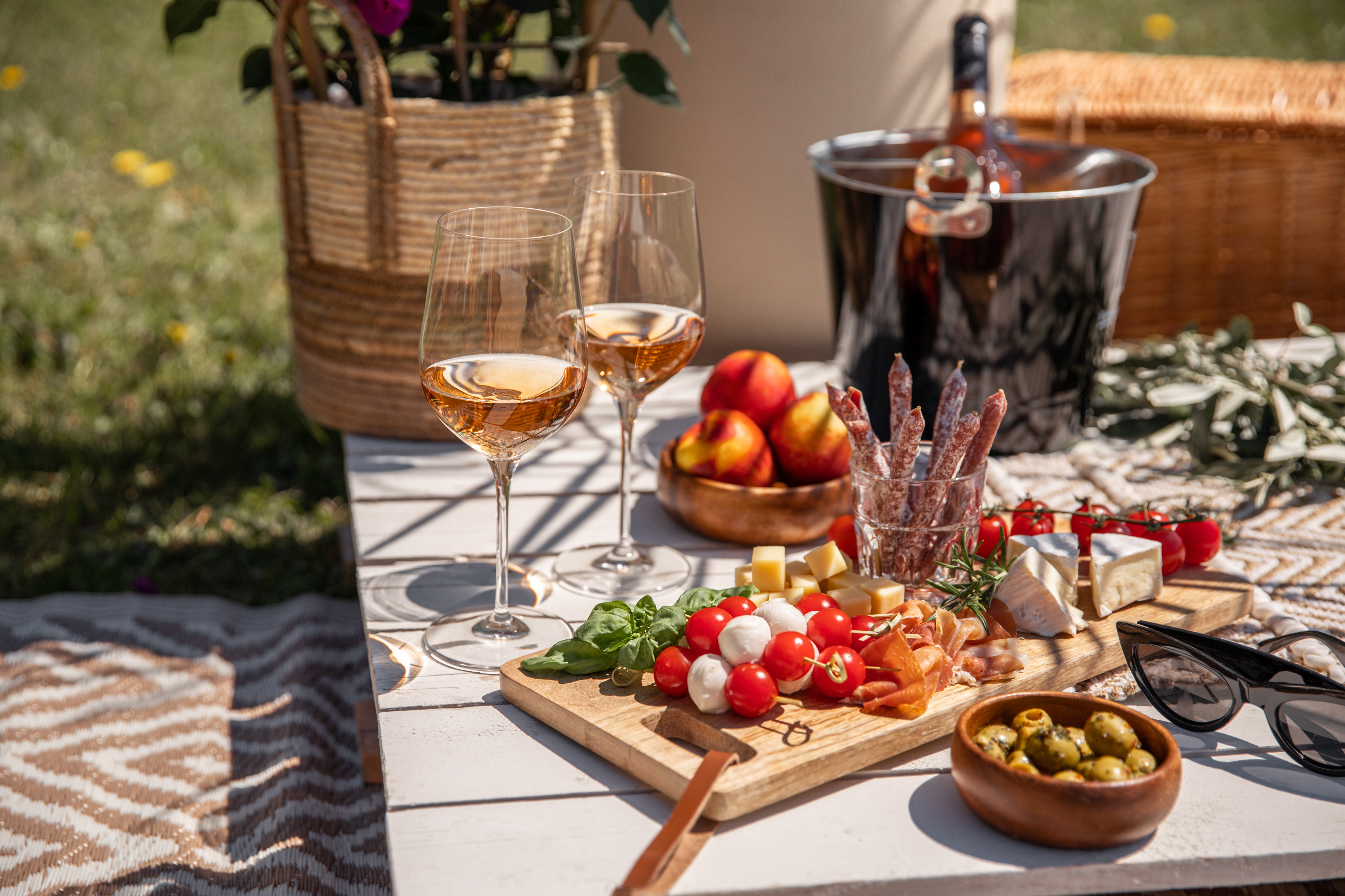 Rose wine glasses with antipasti picnic food snacks on sunny garden party table