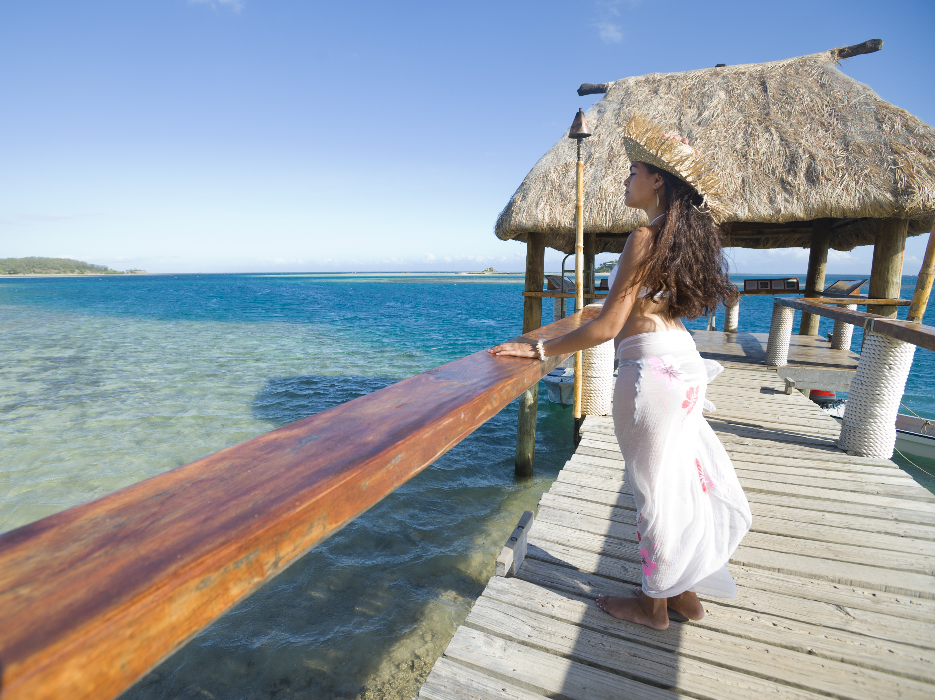 Woman standing on a Jetty on tropical island with grass hut