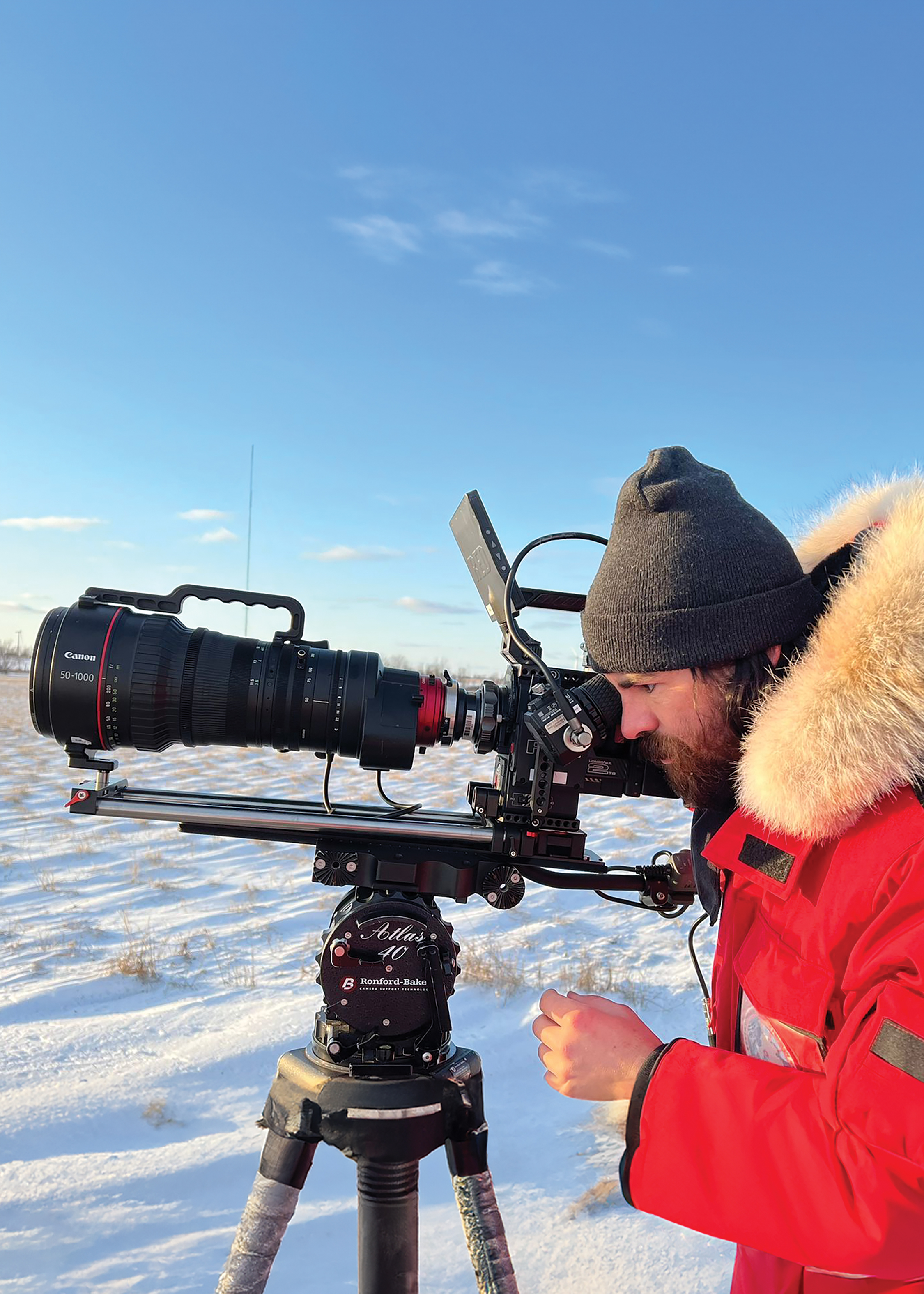 a man in a red parka operates a digital cinema camera in a snowy landscape
