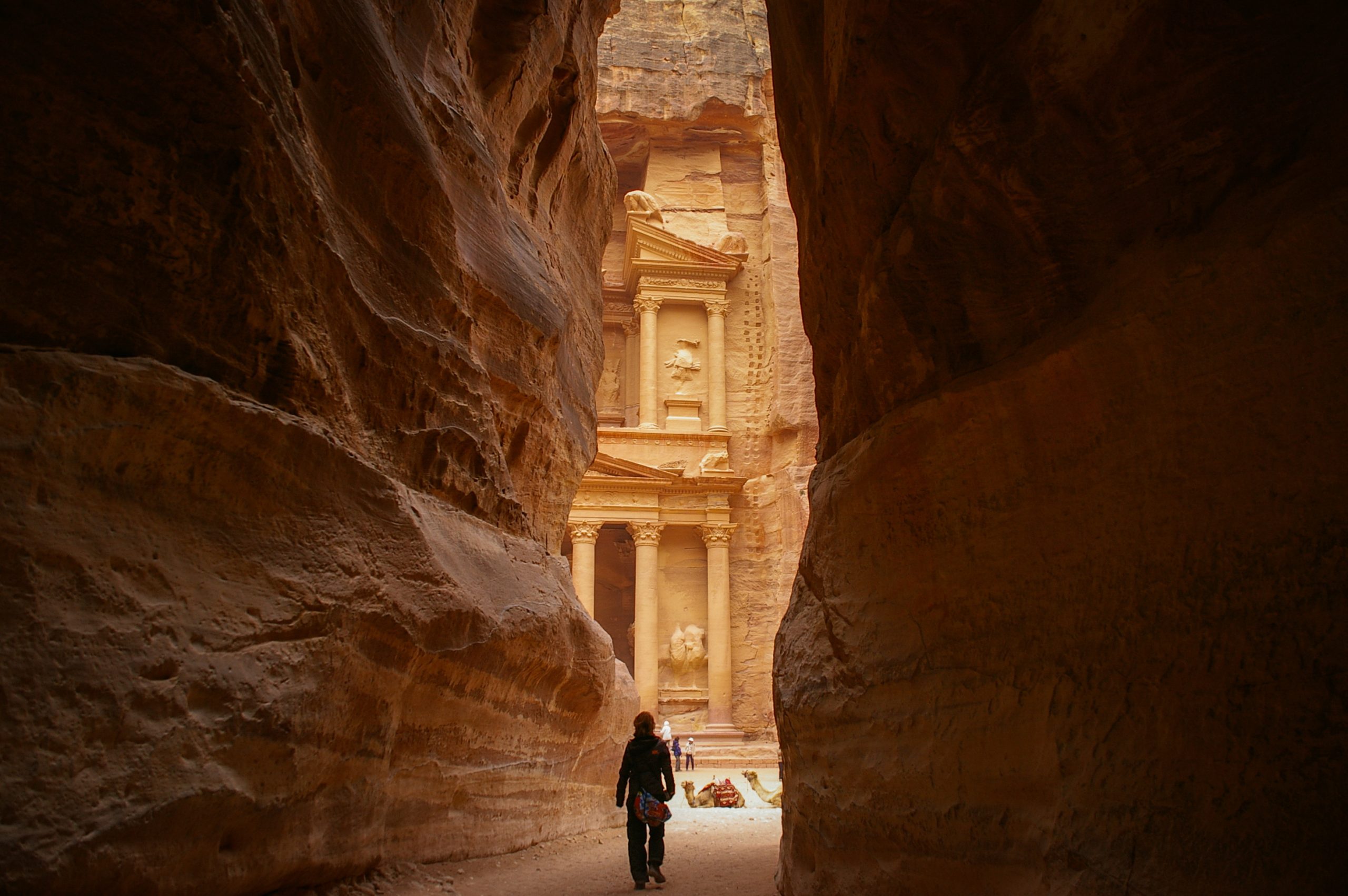 person walking between a crevasse with ruins in background