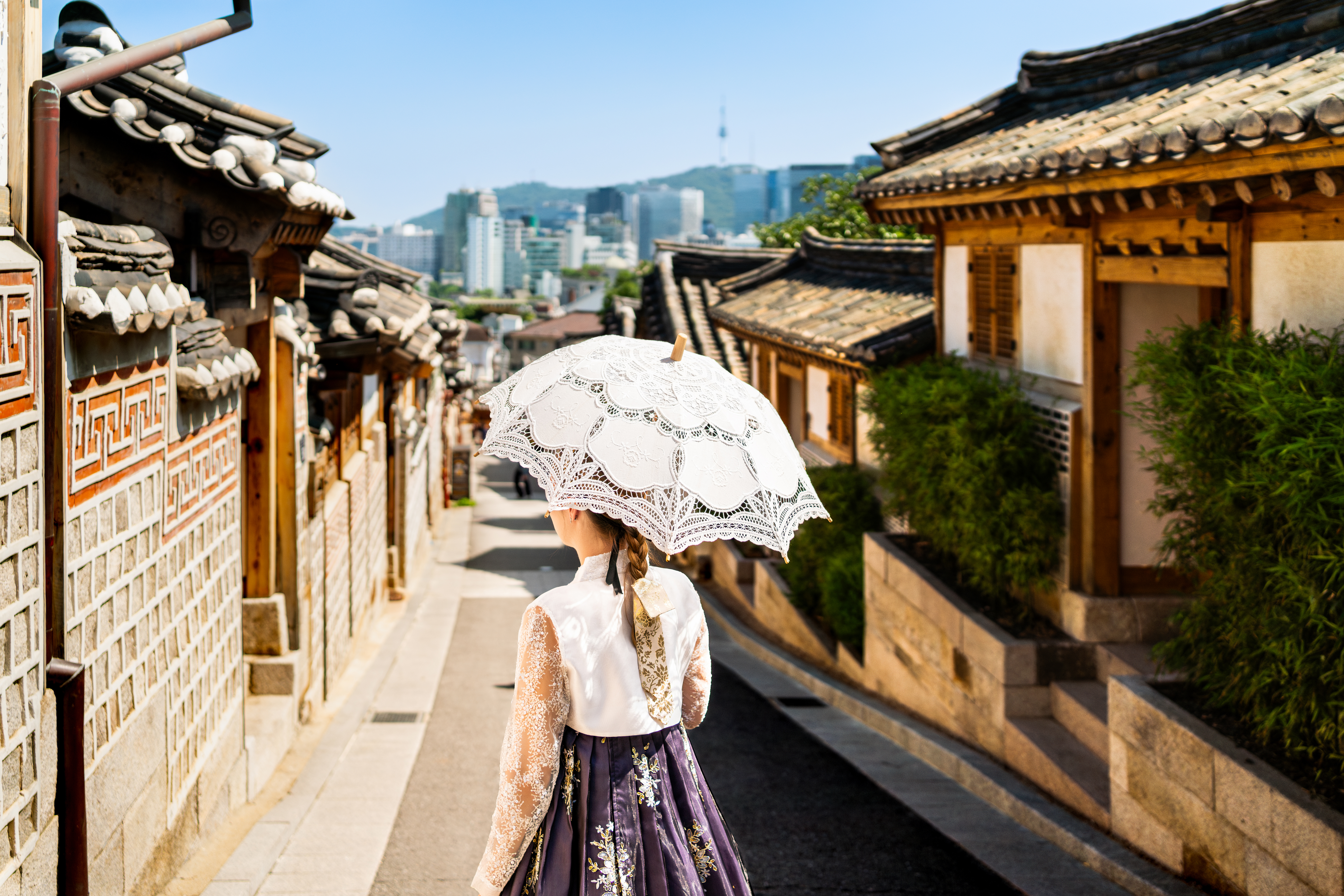 a woman with a parasol and traditional dress walking through Bukchon Hanok Village in Seoul, South Korea