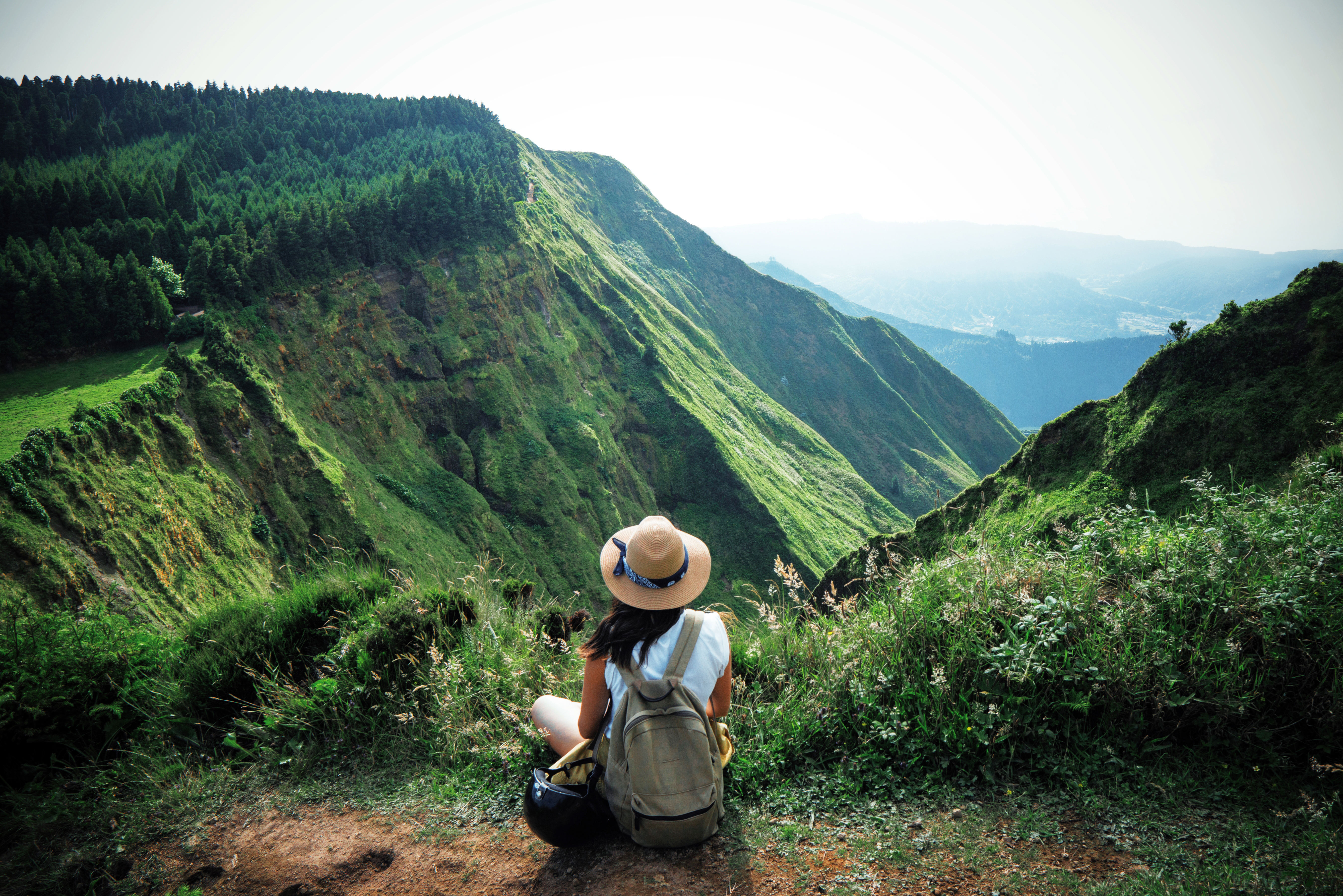 woman sitting on edge of hillside overlooking green mountains