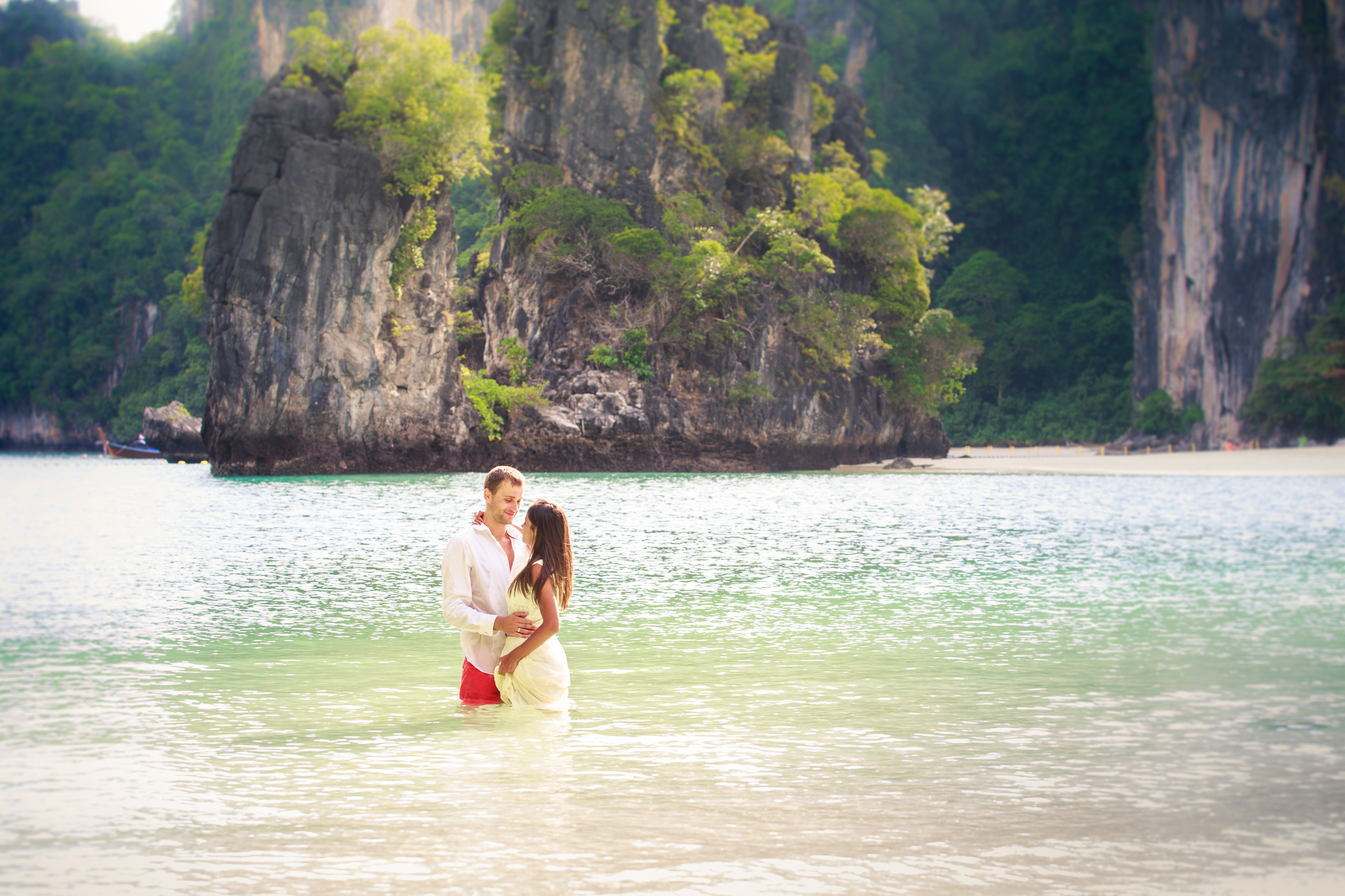 Couple stand in sea water in island bay with karst in background, Thailand
