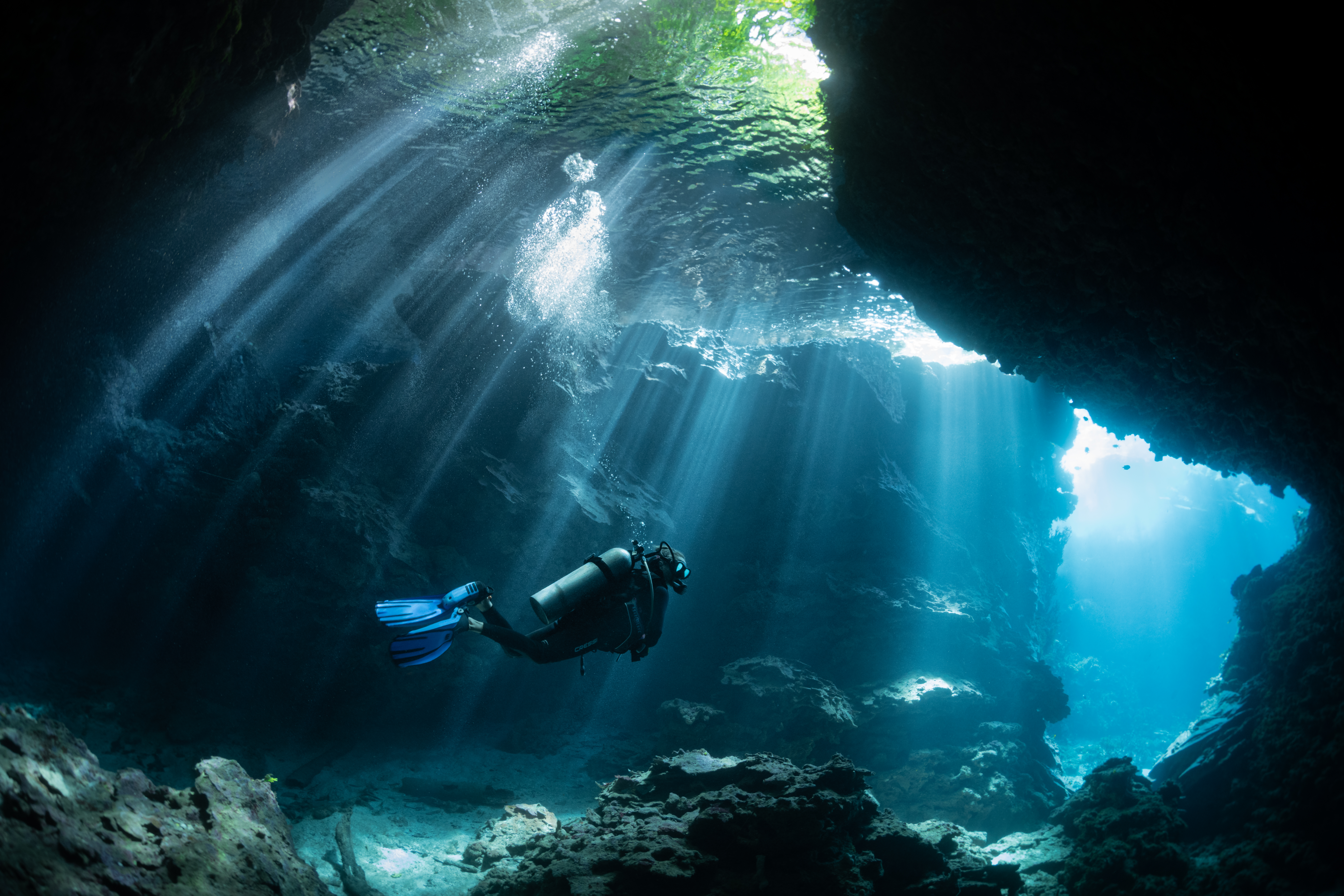 a man scuba dives in the deep waters of the South Pacific with some light breaking through the surface