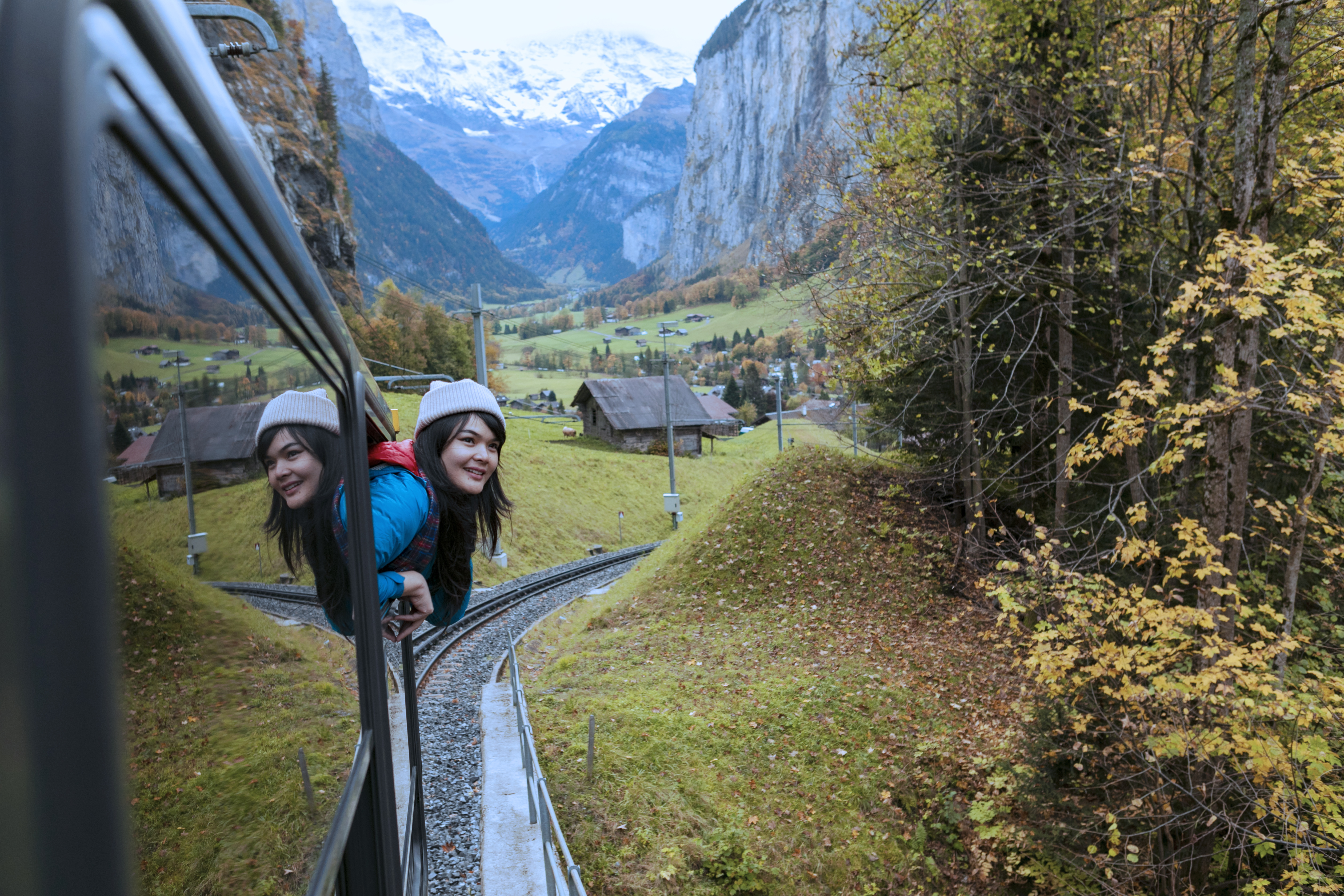 a girl sticks her head outside the window as the train passes through the Swiss Alps