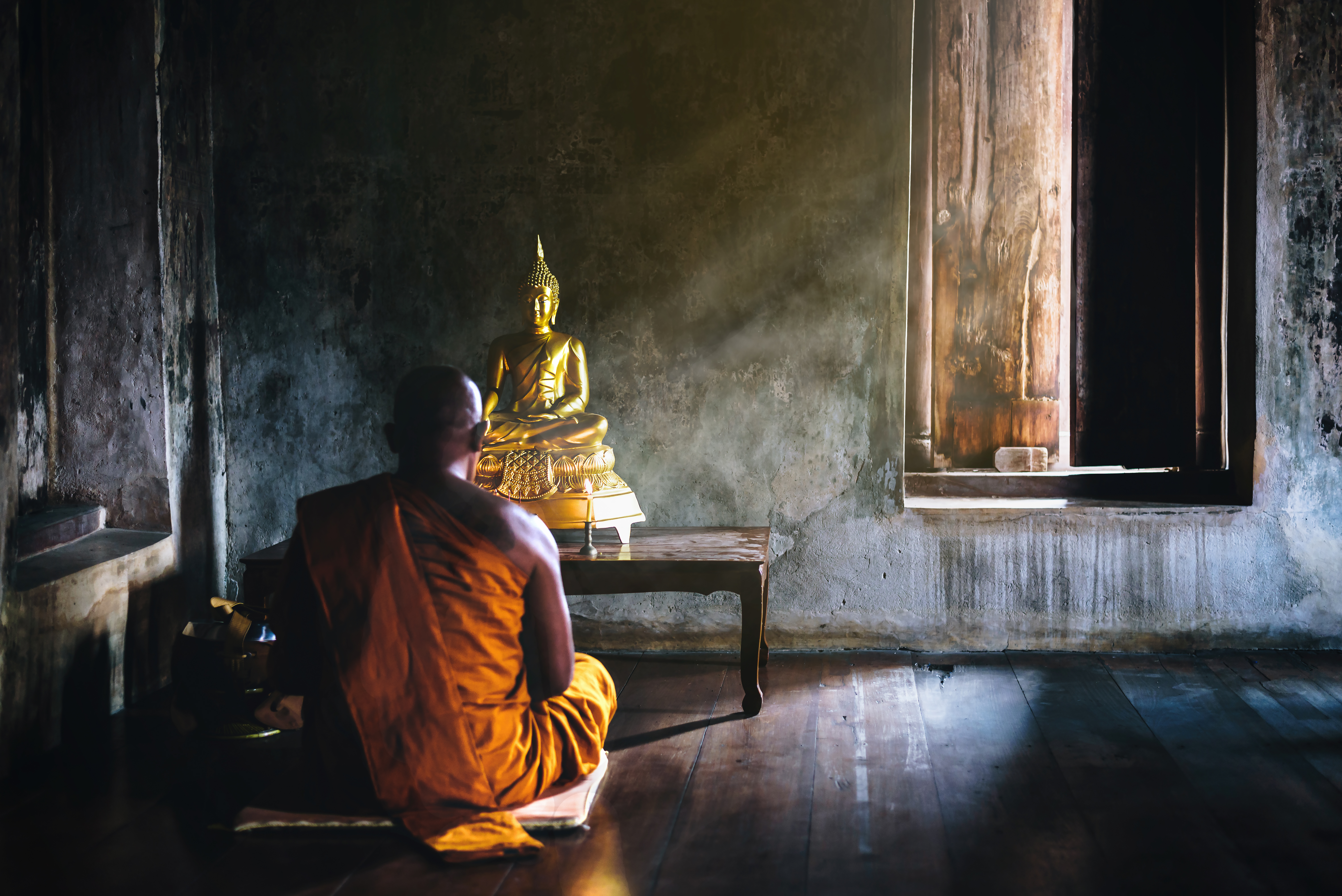 a Buddhist monk meditates in front of a statue of the Buddha in Thailand