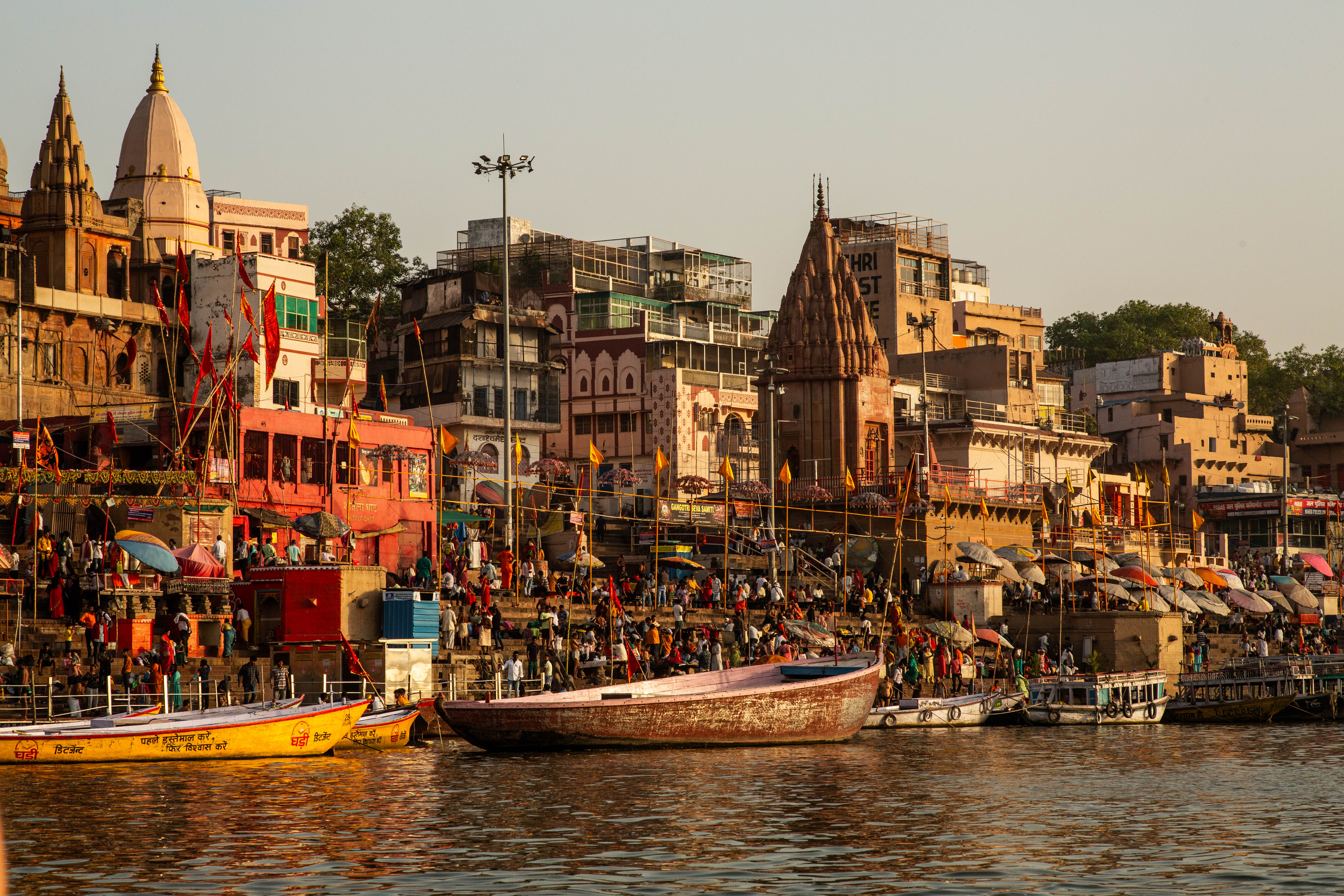 View of the Ganges River with the ghats leading down and boats on the river, as well as pilgrims crowding its edges in Varanasi, India.