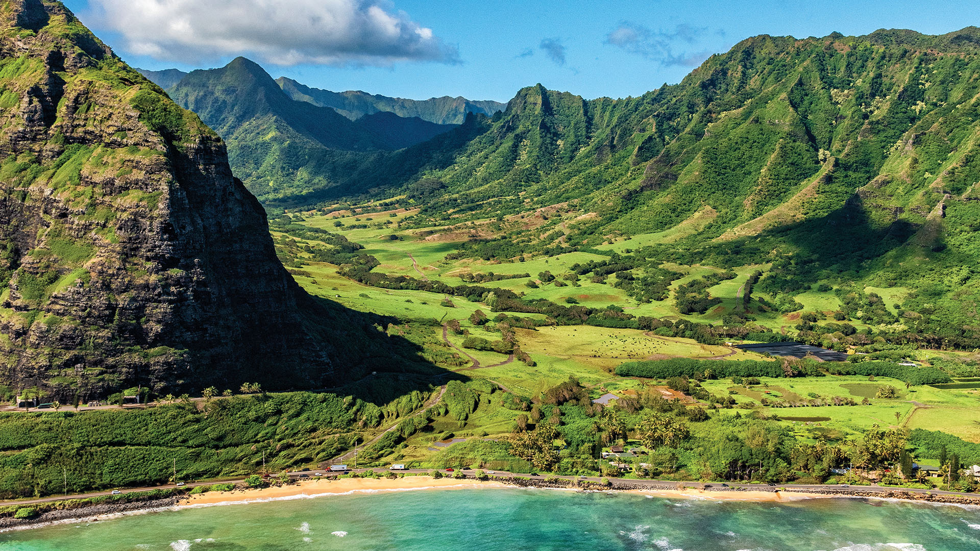 green mountains leading to sandy beach and blue waters in Hawaii