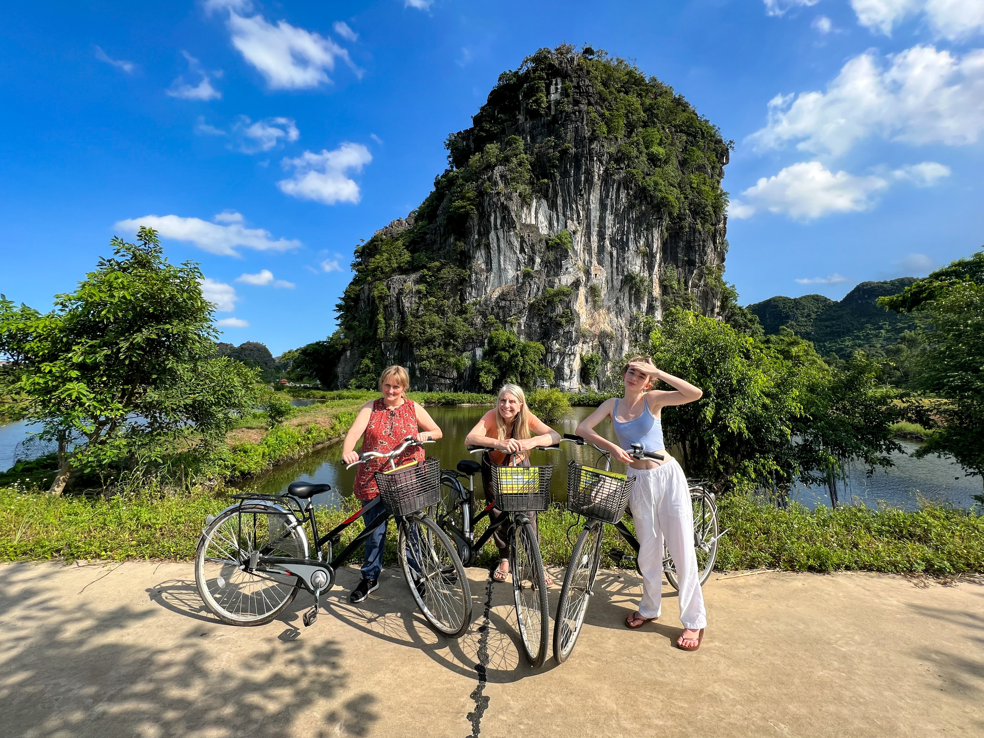 A group of women pose with their bikes in front of limestone hills in Ninh Binh, Vietnam.