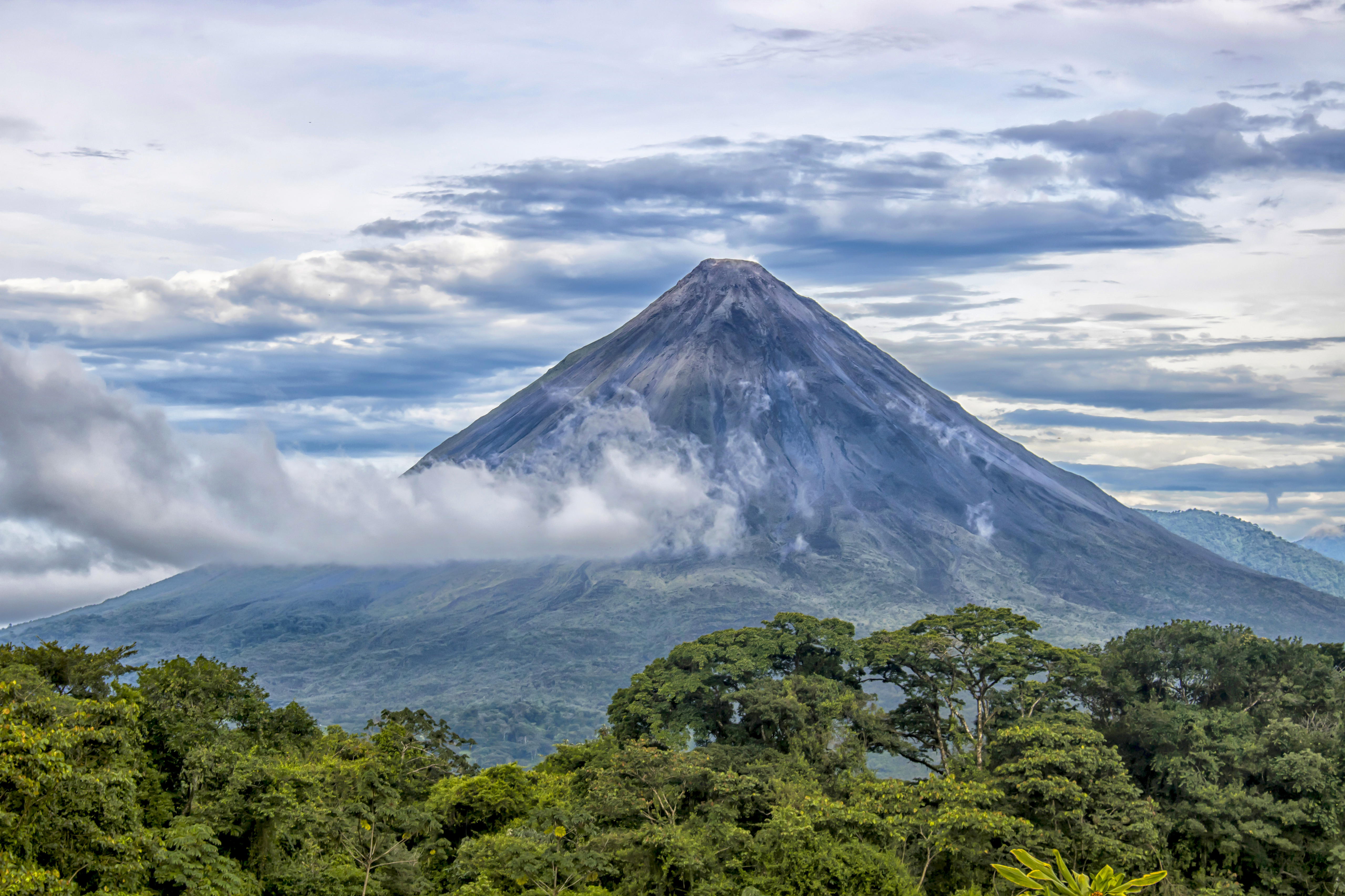 Rainforest, volcano rising in distance with clouds surrounding