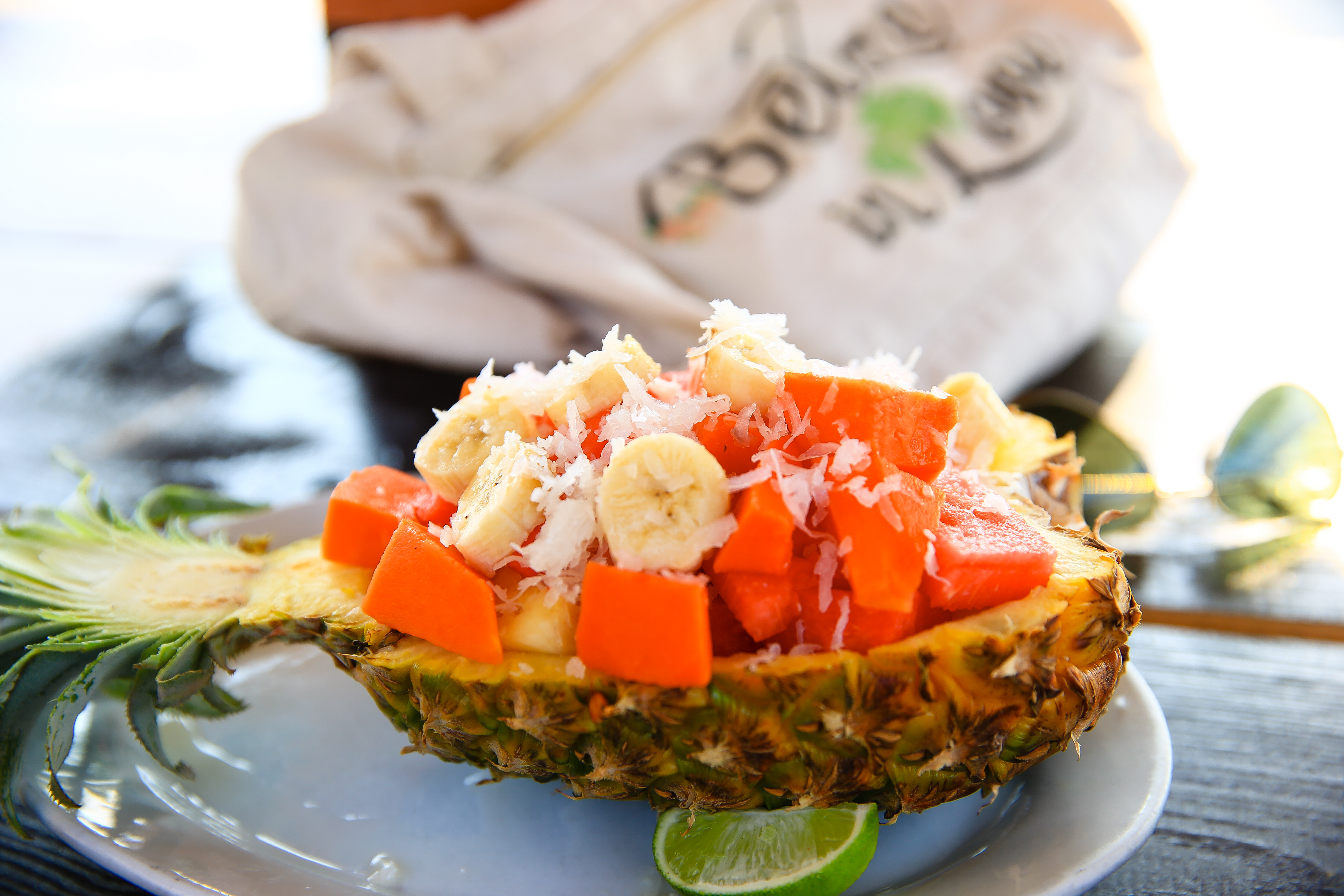 A halved pineapple filled with banana, papaya, and coconut shavings, with a lime slice on a plate.