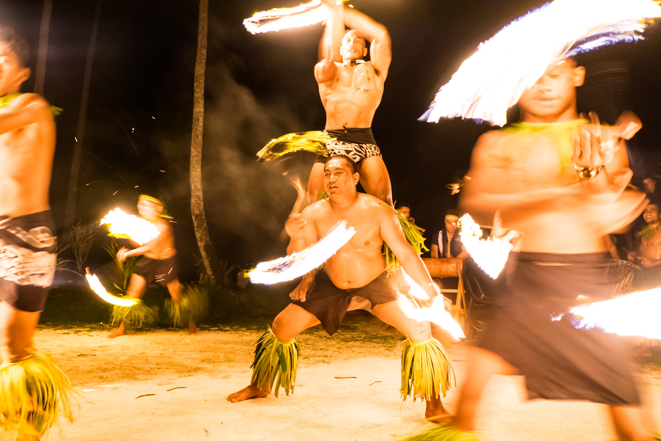 Fire dancers perform rhythmic movements under the night sky, creating glowing trails with flaming torches.