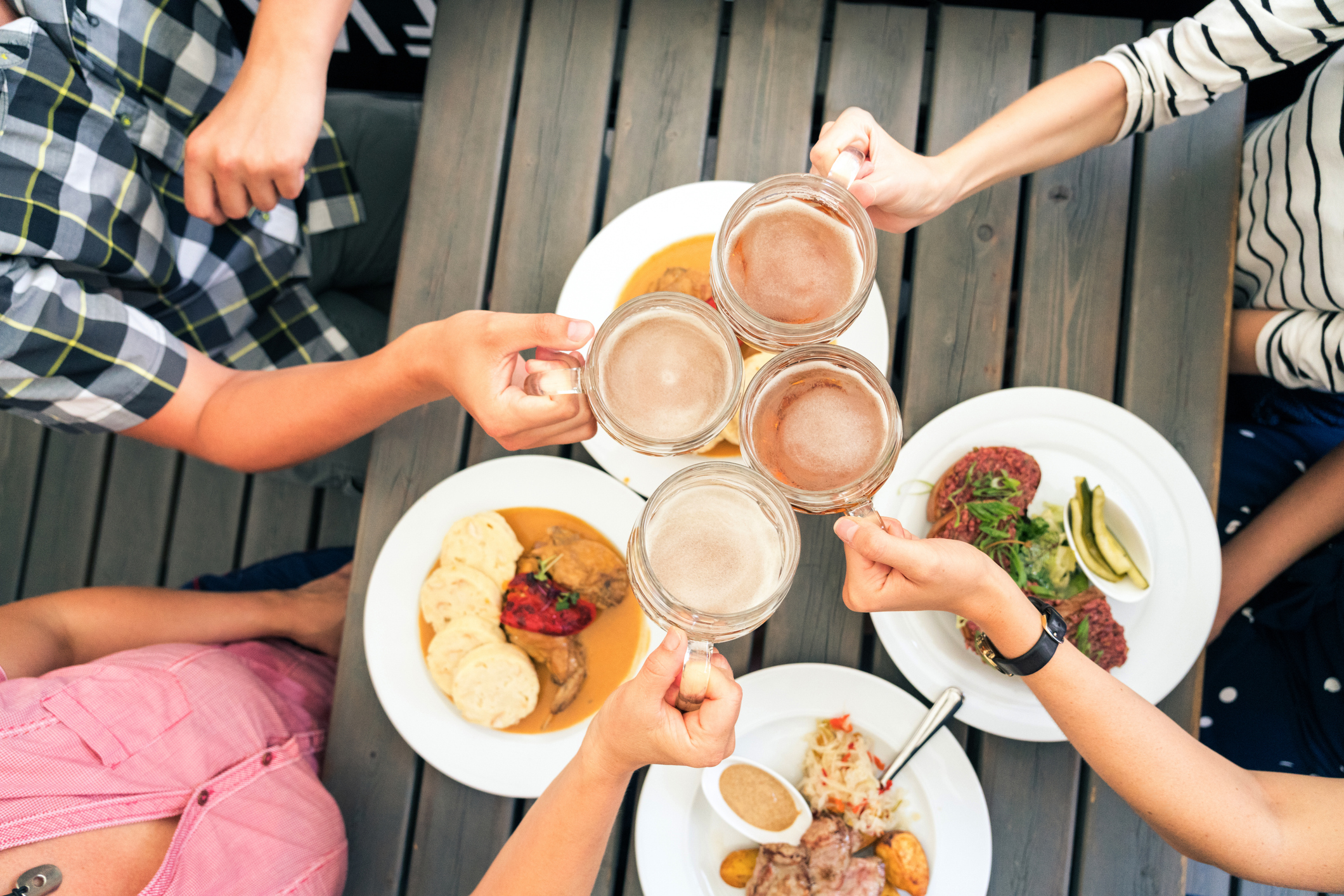Friends toasting with beer mugs over a table of diverse dishes, enjoying a meal together.