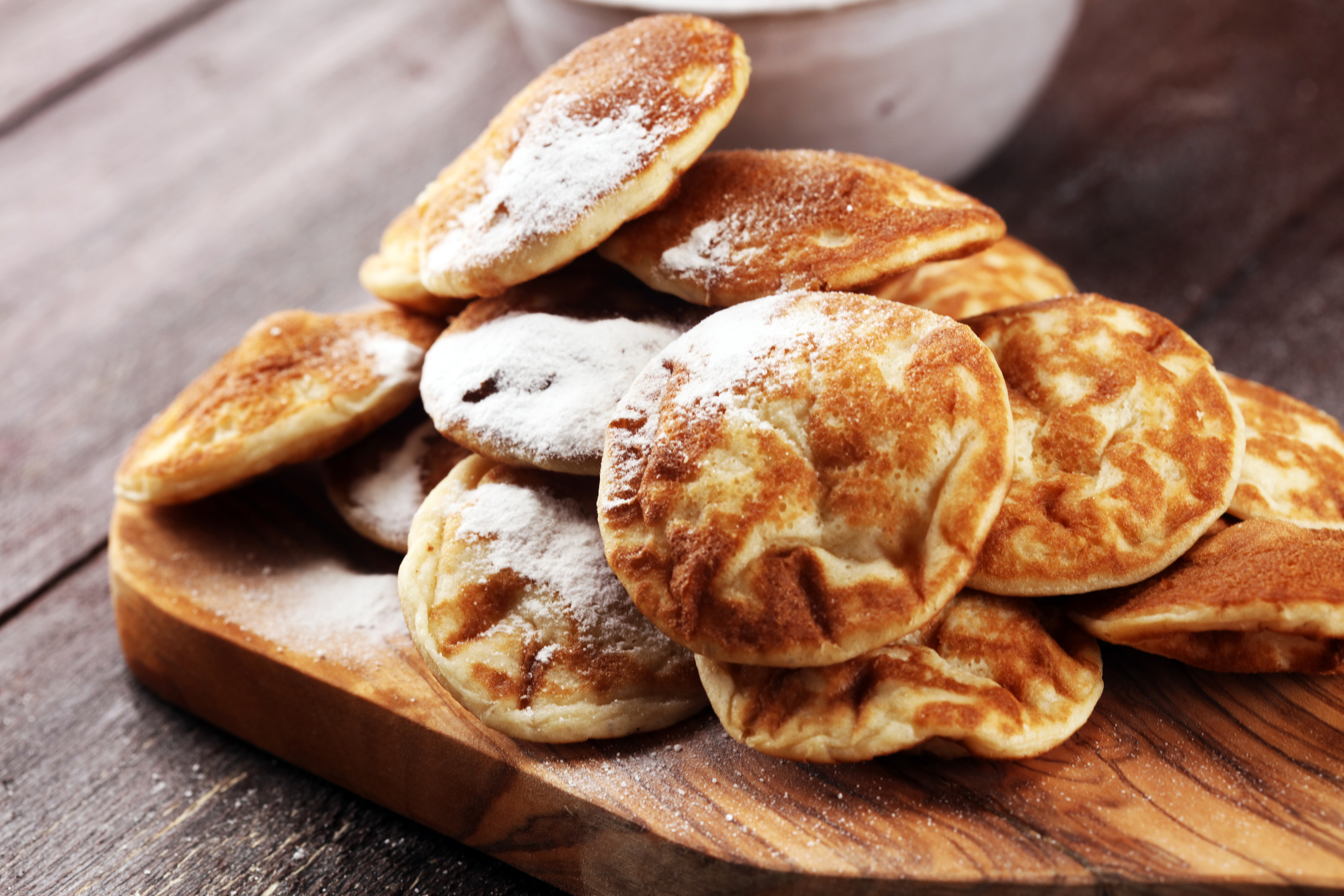 A pile of fluffy, round pancakes dusted with powdered sugar on a wooden cutting board.