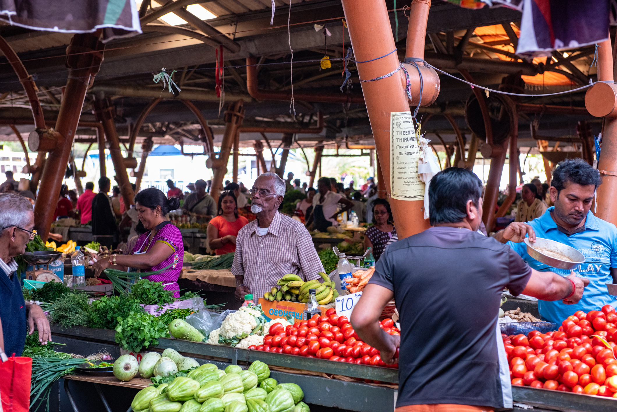 A vibrant market scene with people shopping for fresh vegetables and fruits at various stalls.
