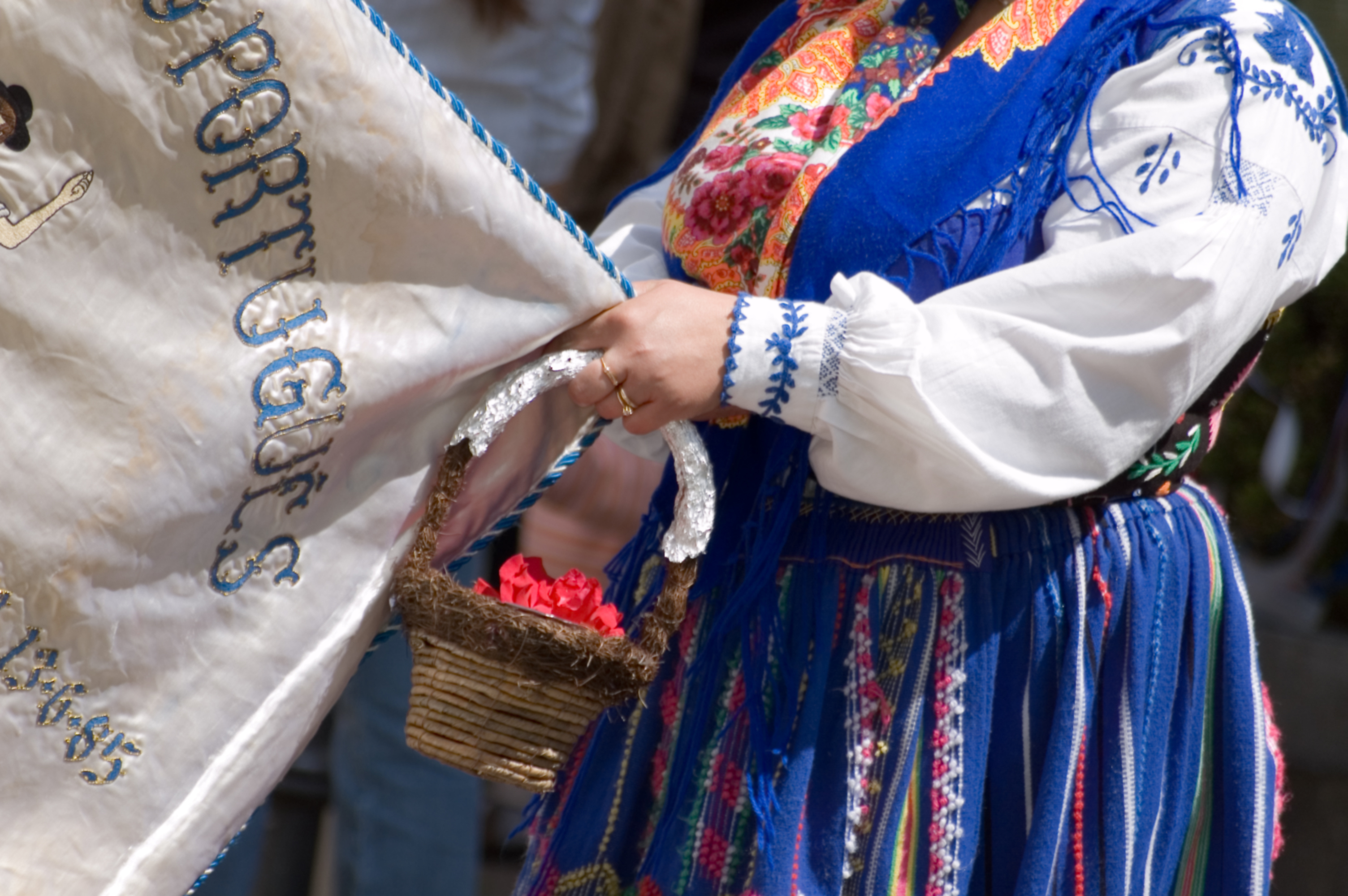 A person in traditional clothing holds a banner and a small basket of flowers during a cultural event.