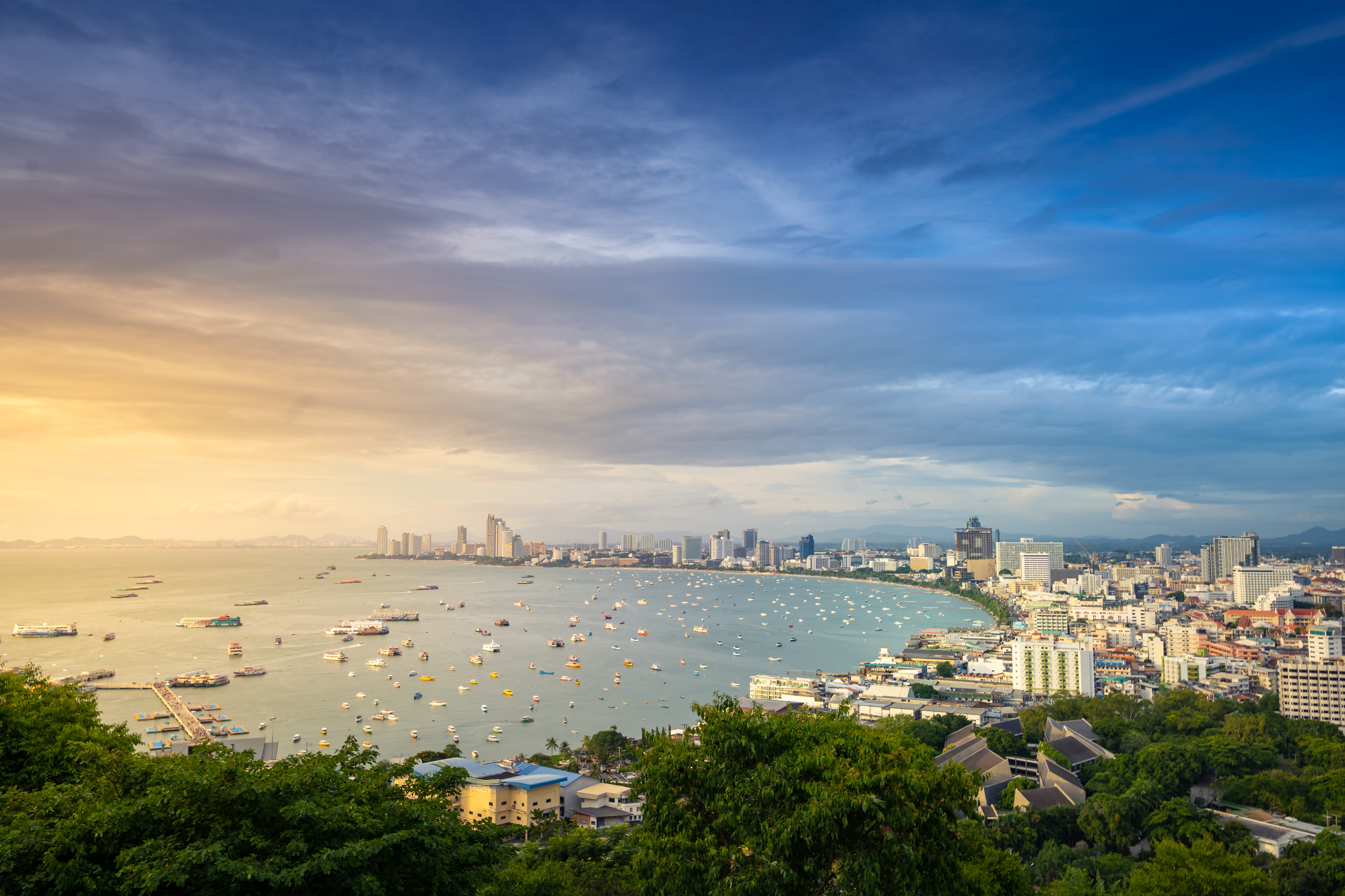 Arieal sunset view of boats in water and buildings along curved coastline of Pattaya city