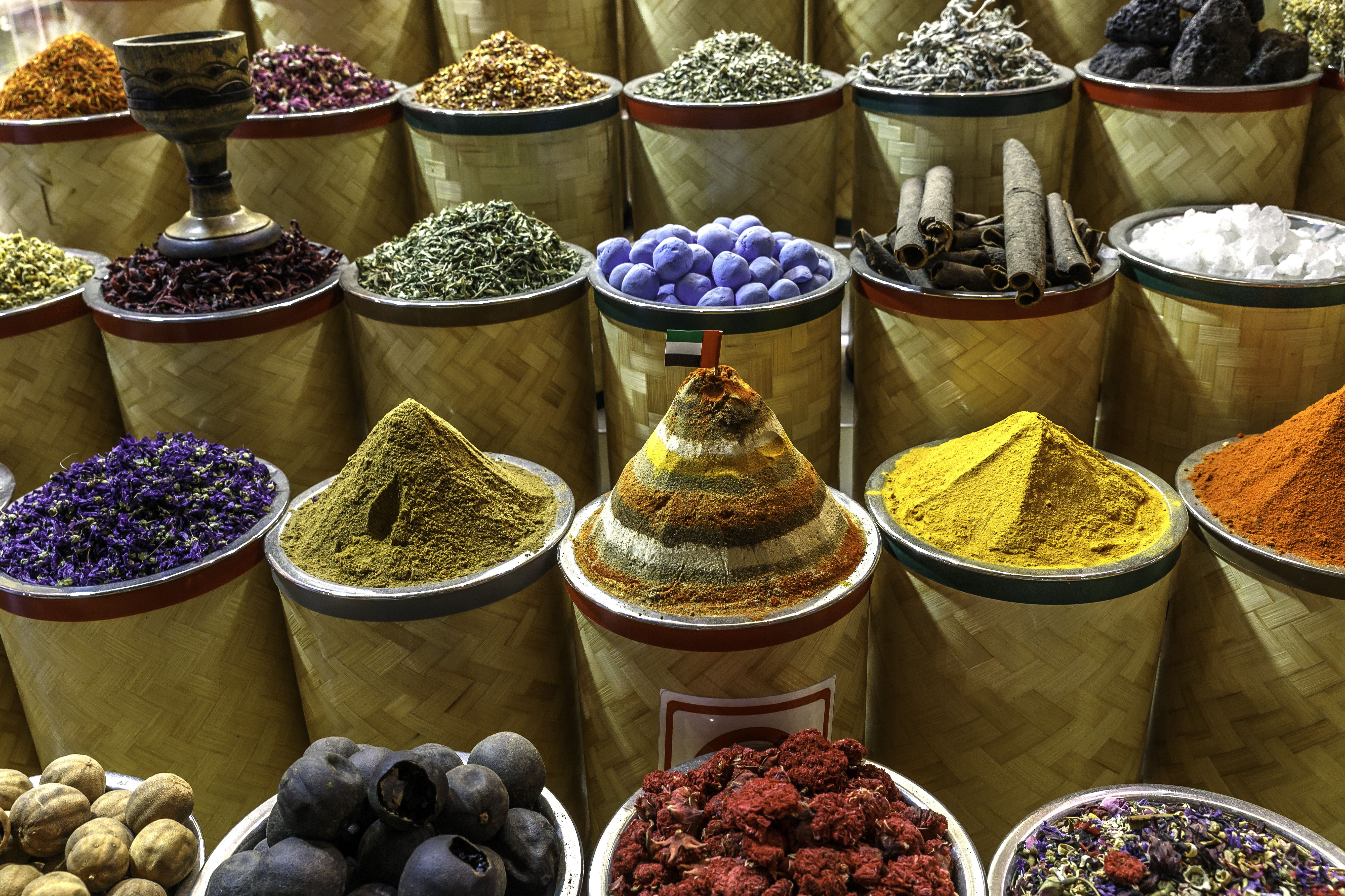 Colorful spices and herbs in cylindrical containers, arranged in rows, showcasing various textures and vibrant hues.