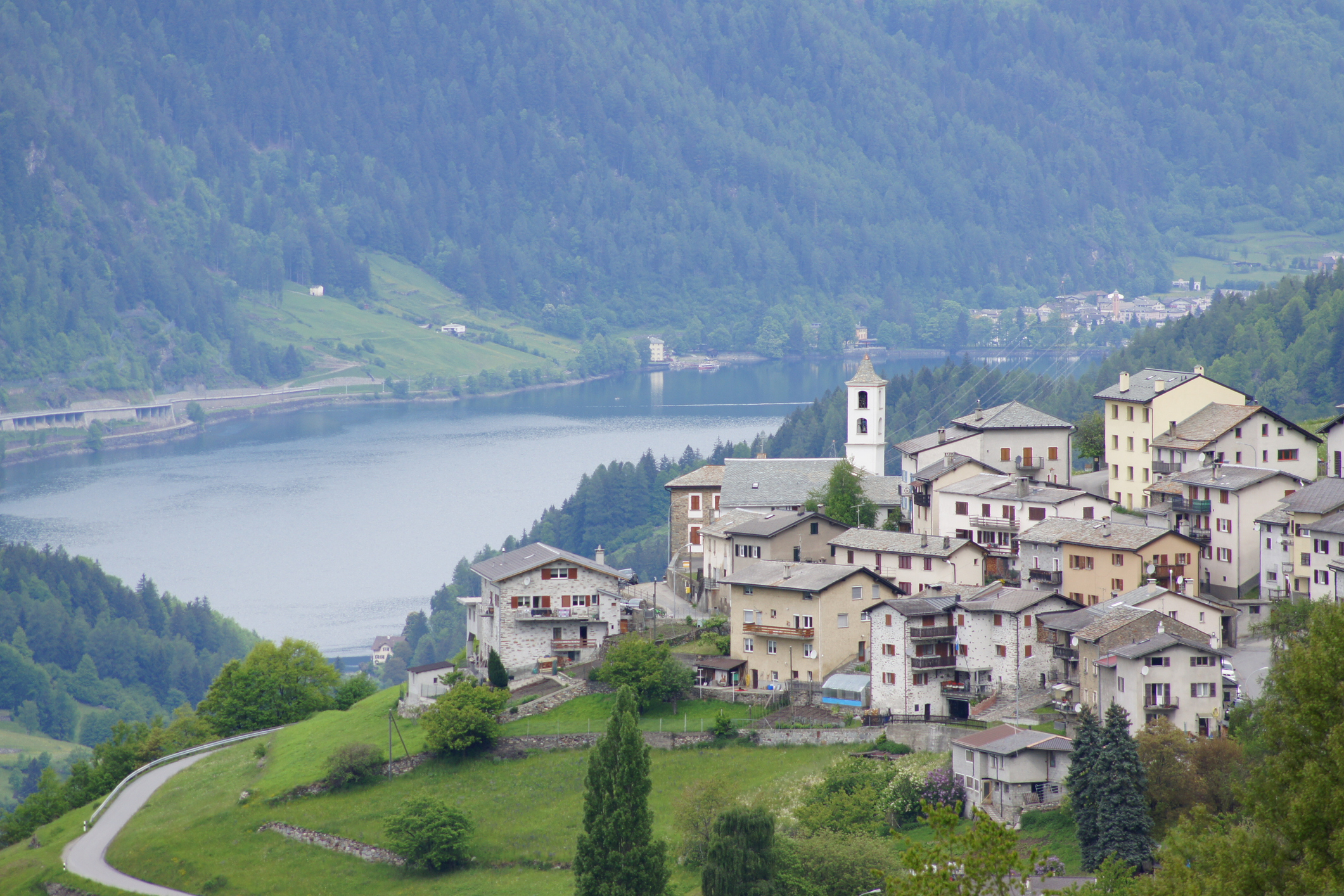 Scenic view of a quaint village on a hillside, overlooking a lake surrounded by green mountains.