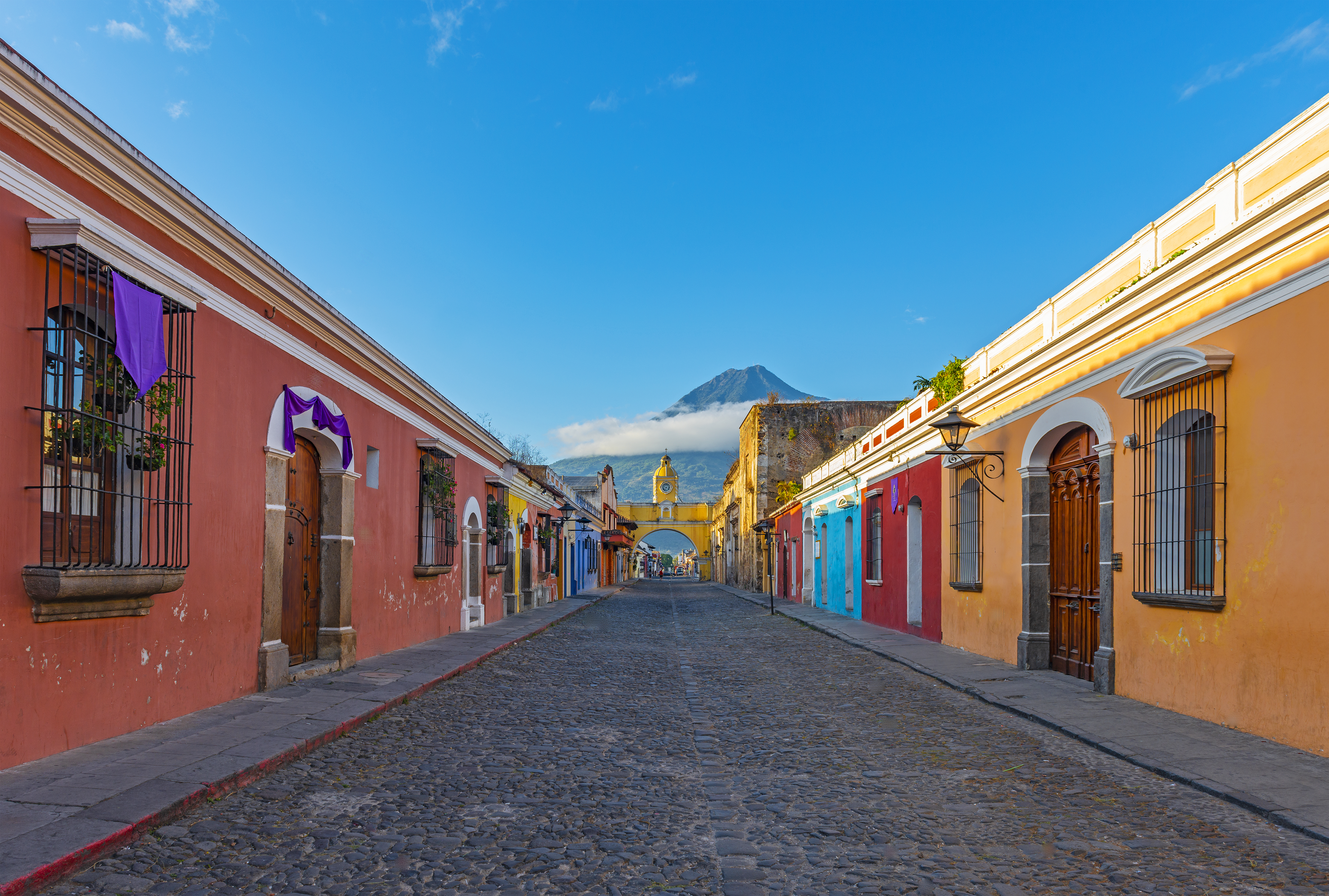"Colorful main street of Antigua city at sunrise with the famous yellow arch and the Agua volcano in the background "