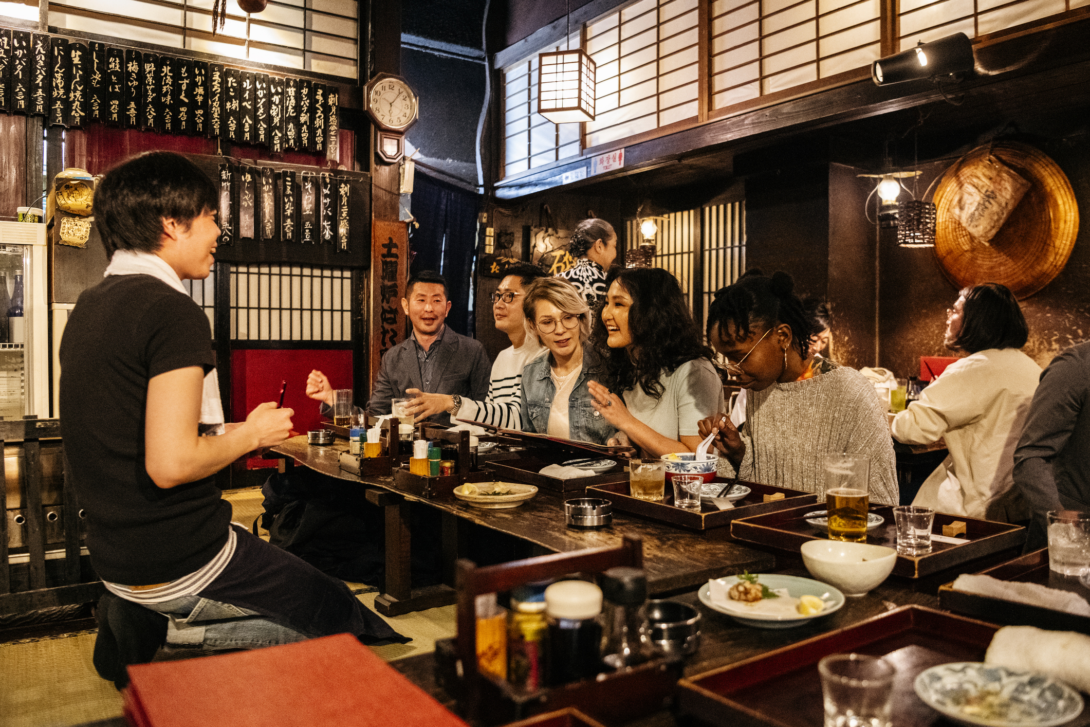 Group of friends dining together in a cozy restaurant, enjoying food and drinks, with warm lighting and traditional decor.