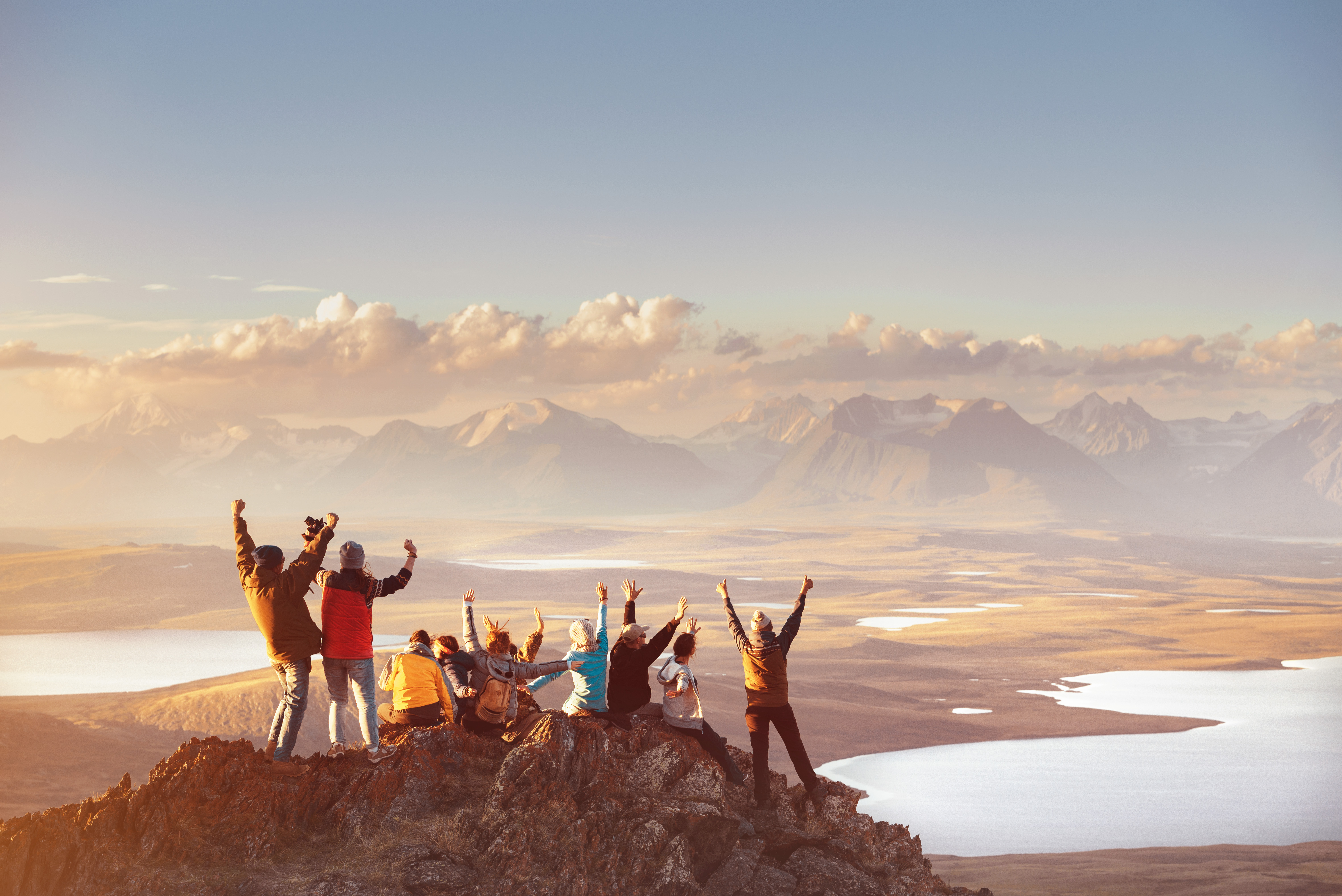 Group celebrating hiking to reach top of mountain top looking out at mountain's valley
