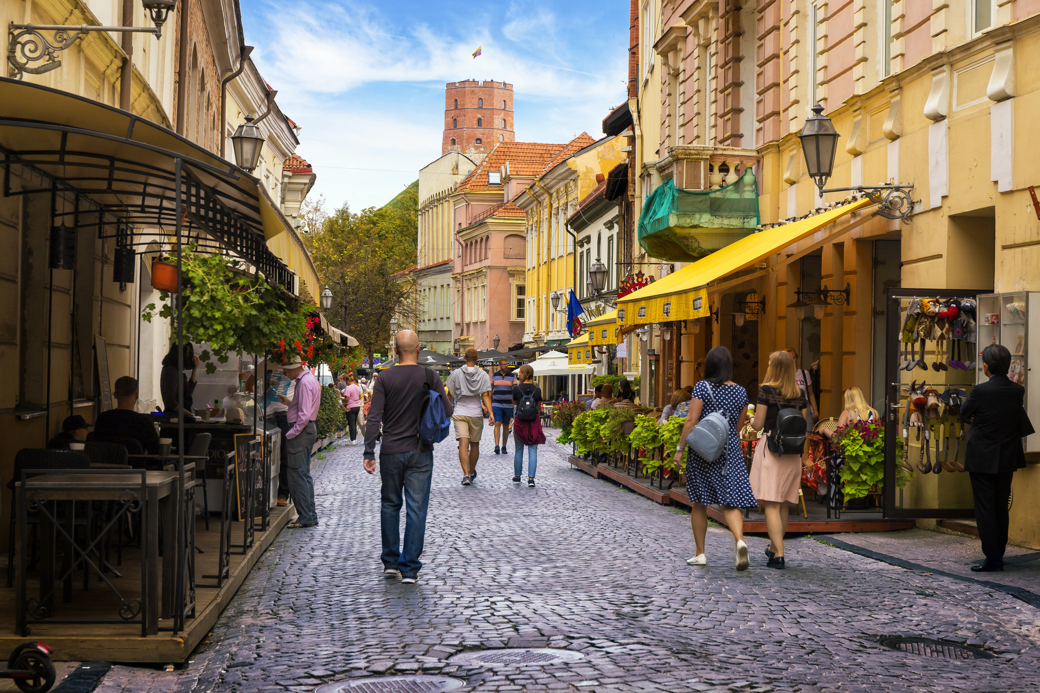 Charming cobblestone street lined with shops and cafes, bustling with pedestrians under a blue sky.