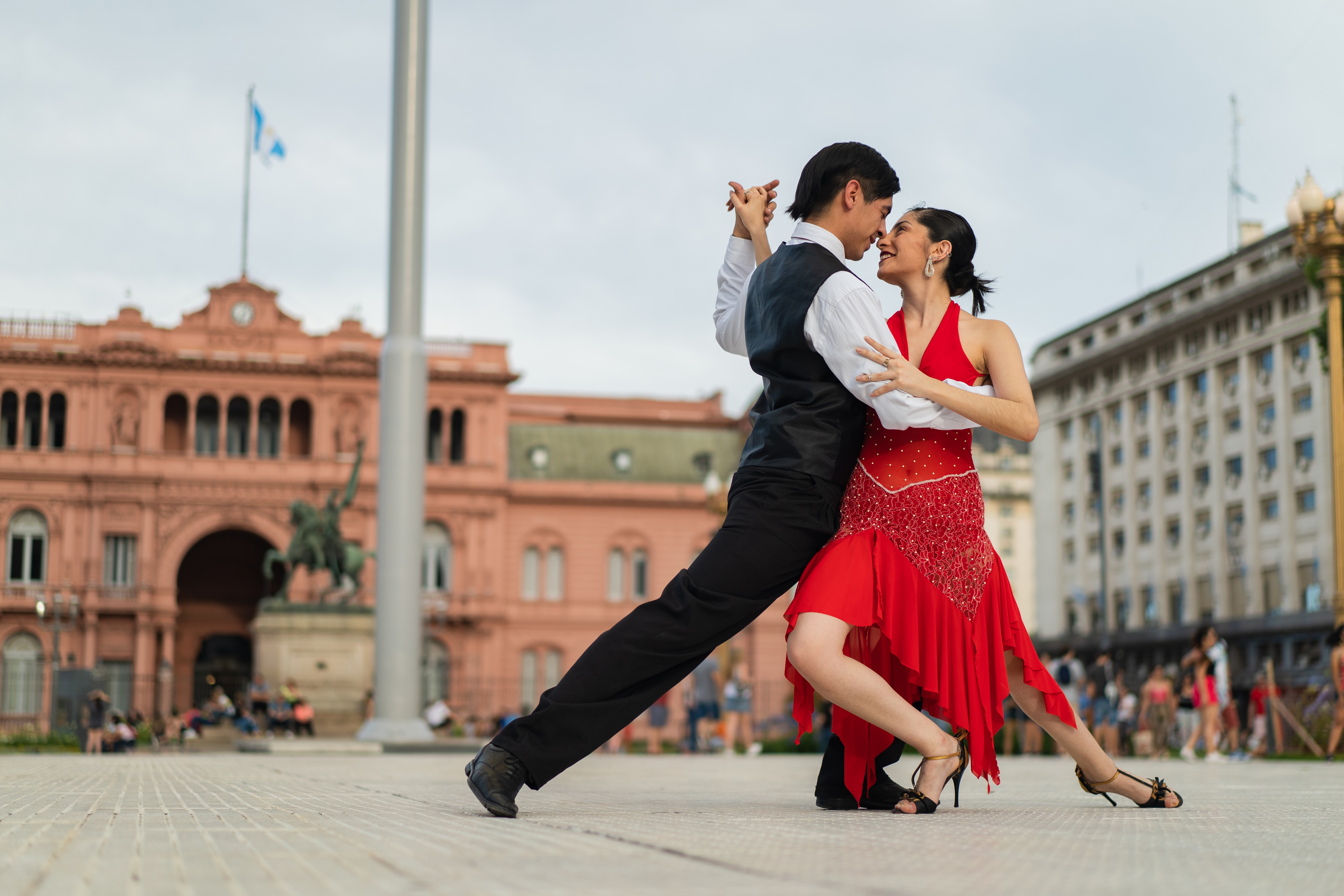 A couple dances tango in front of a historic building, showcasing their passion and elegance in a vibrant outdoor setting.