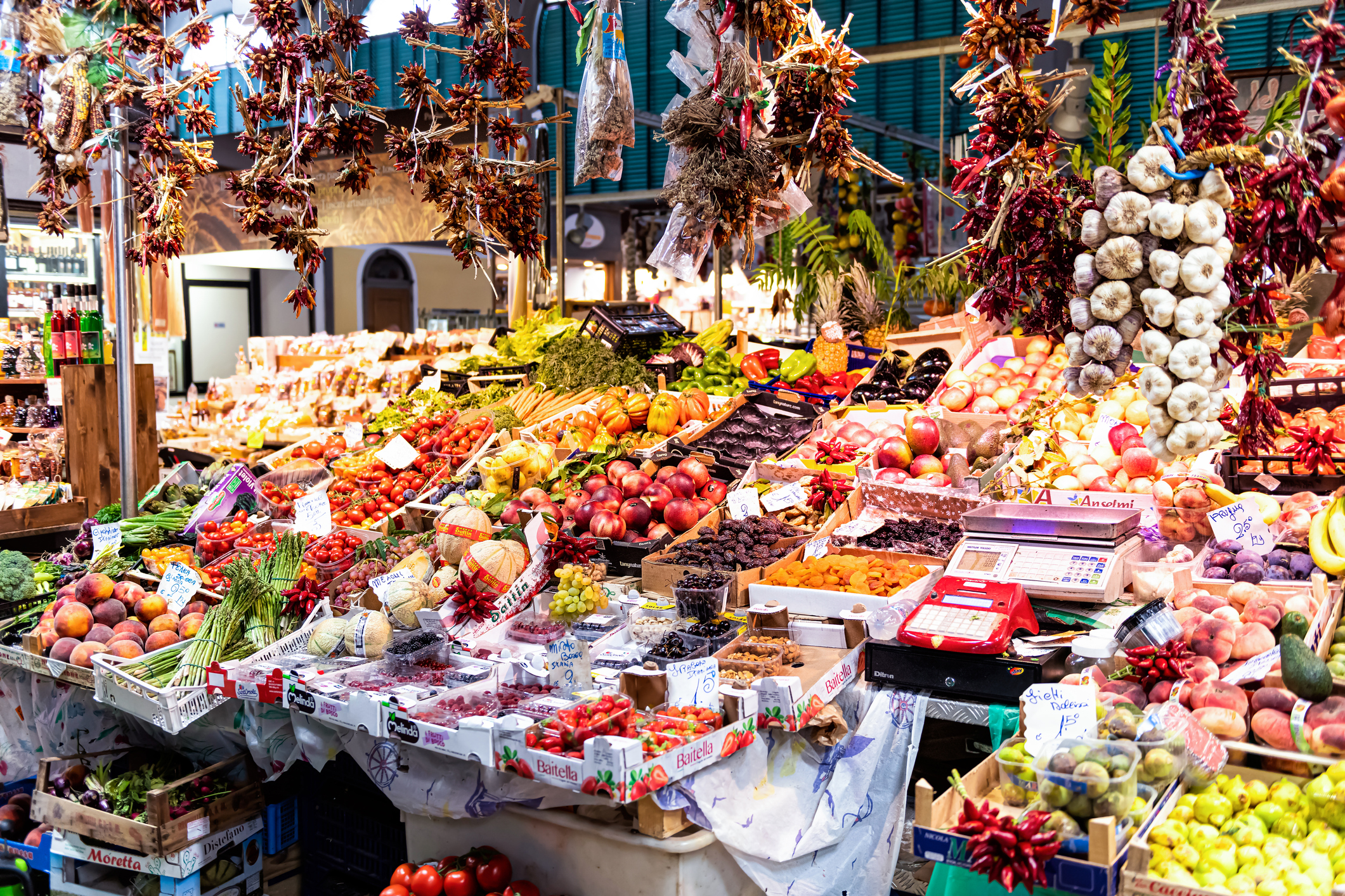 Vibrant market scene filled with colorful fruits, vegetables, and hanging spices displayed on various stalls.