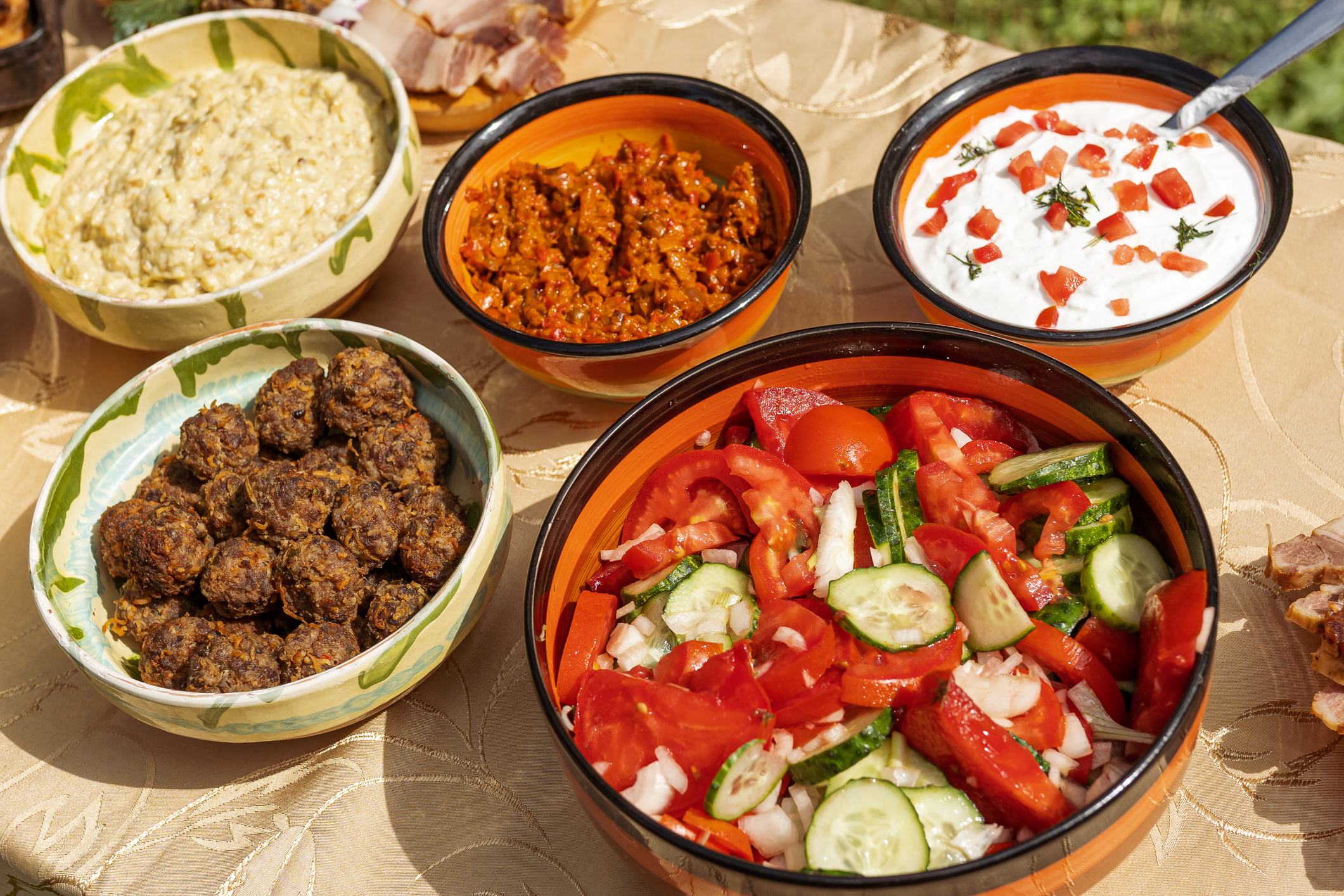 A spread of colorful dishes on a table, including salads, dips, and meatballs in bowls.