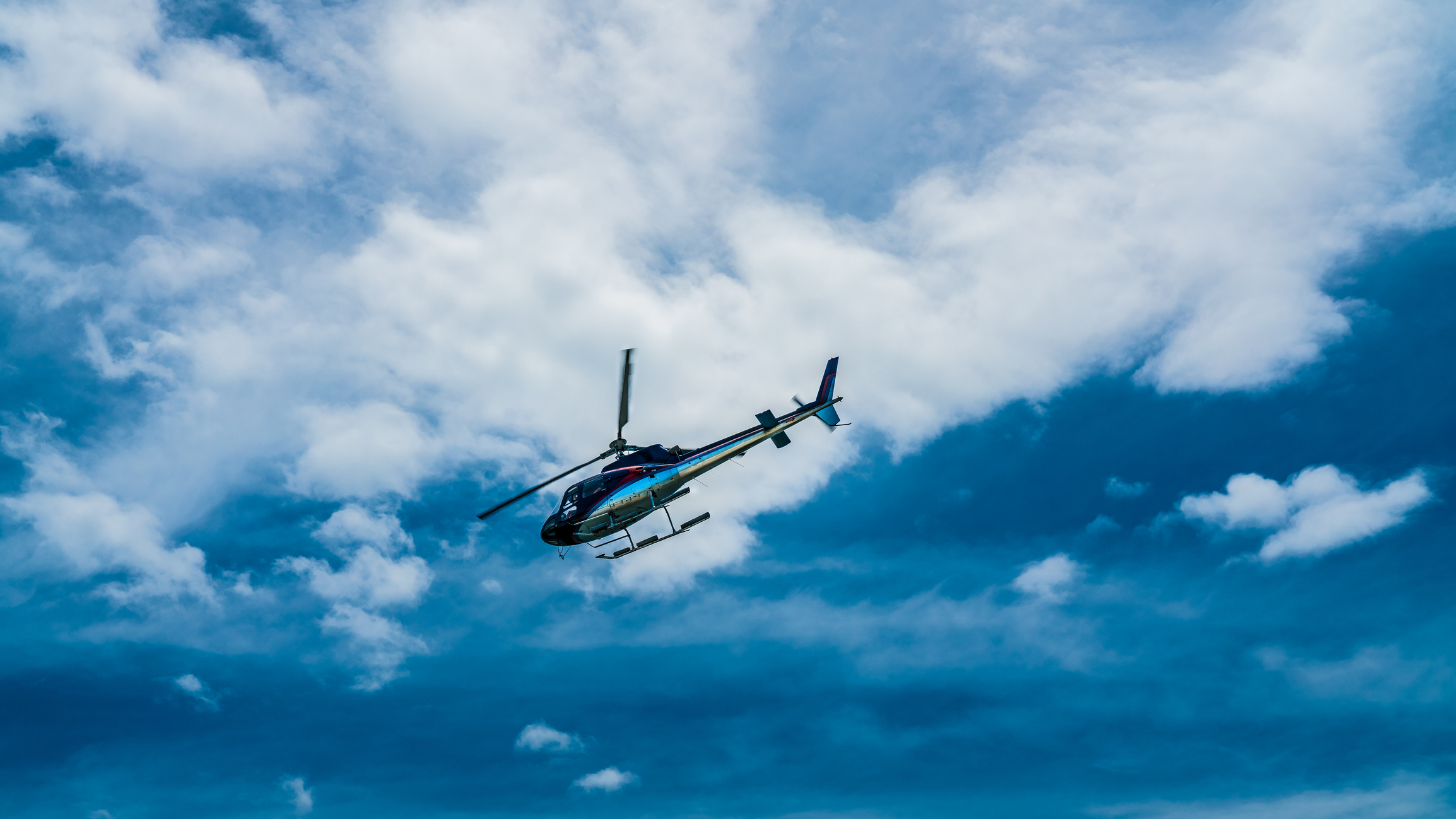 A helicopter flying against a backdrop of blue sky and fluffy white clouds.