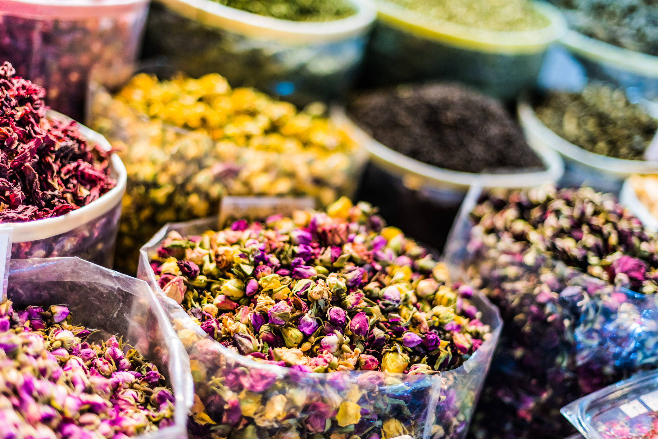 Colorful dried flower petals in transparent containers at a market, showcasing a variety of textures and hues.