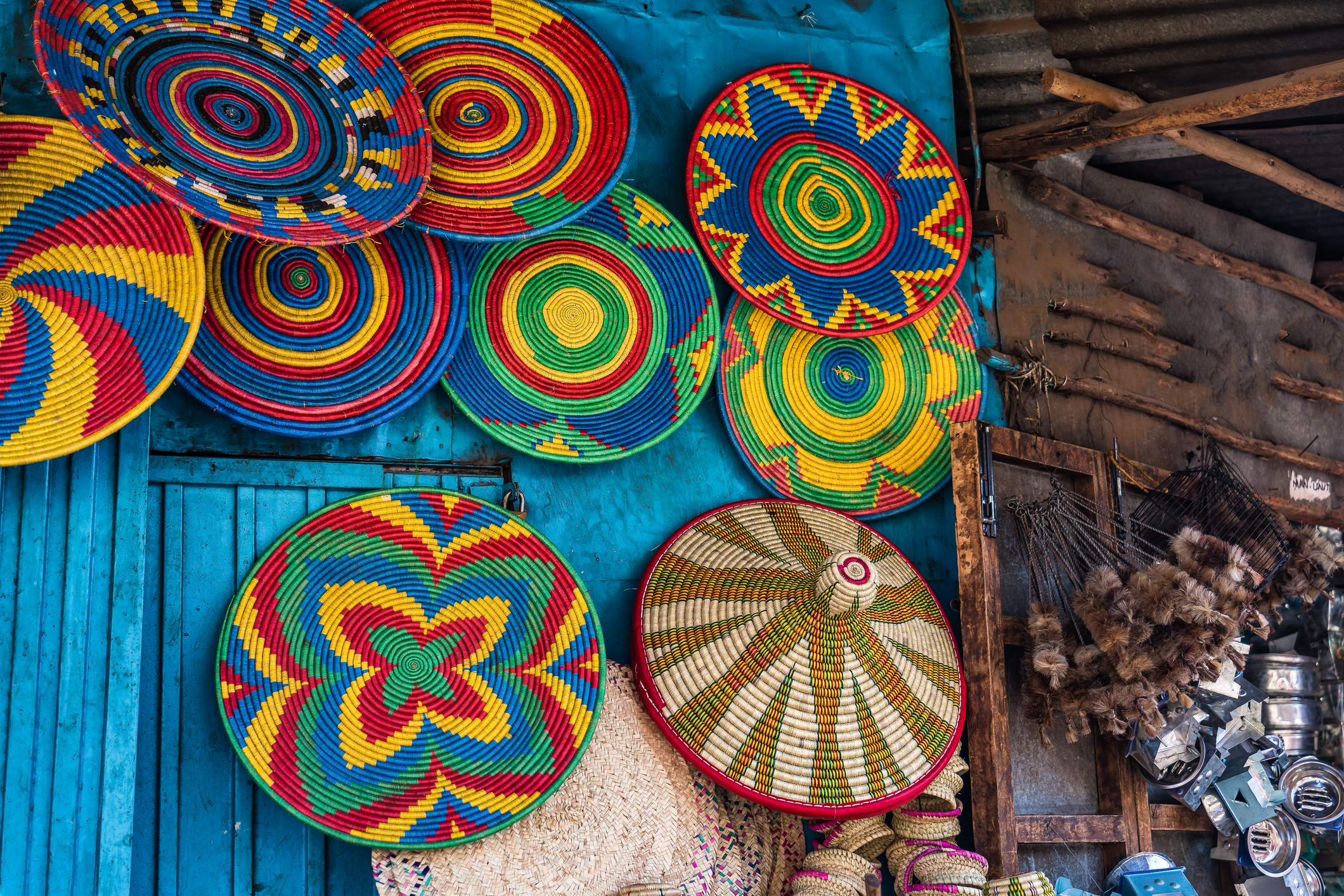 Colorful woven baskets hang against a blue wall, showcasing intricate patterns and vibrant colors in a market setting.