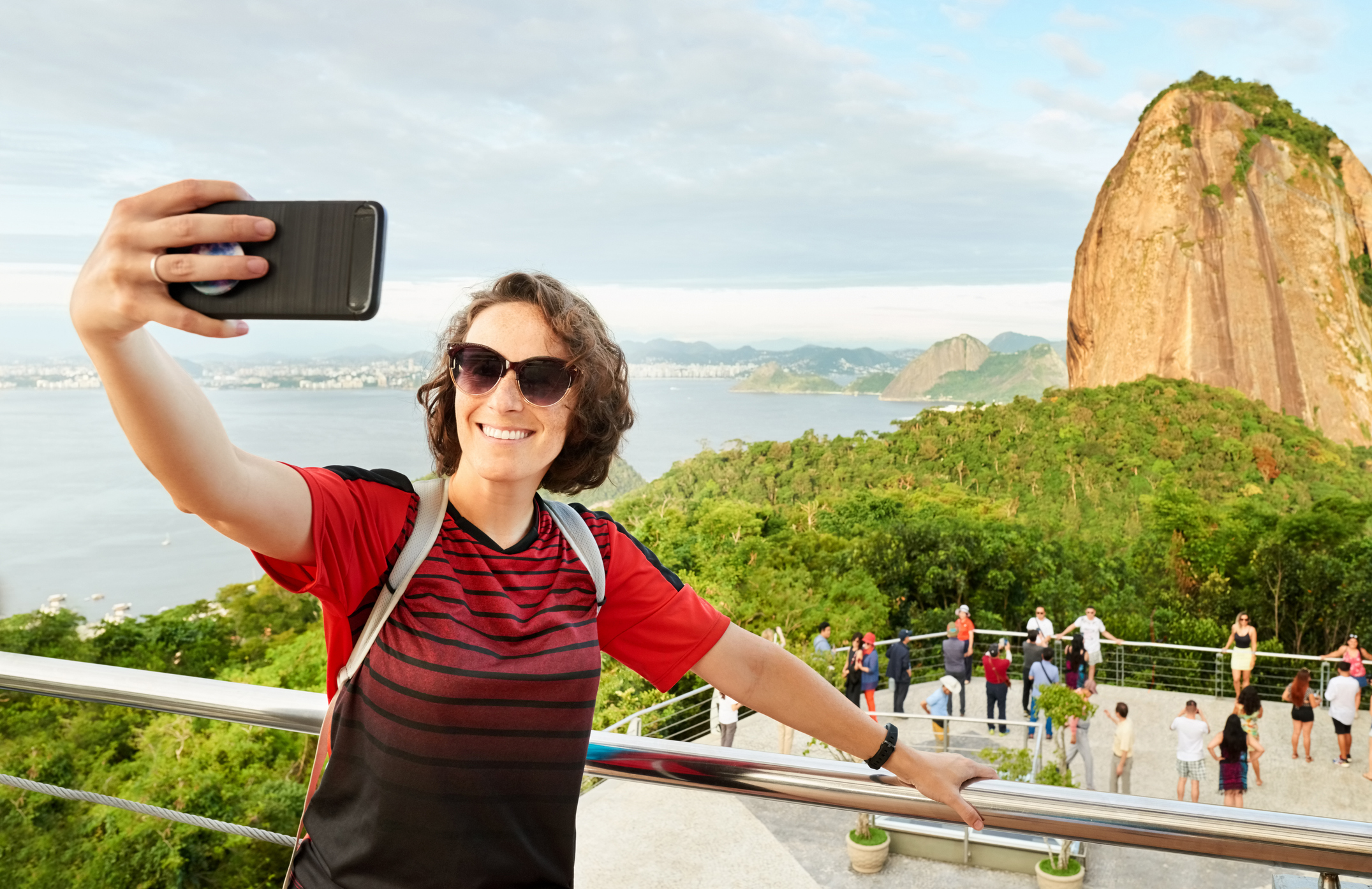 Person taking a selfie with a scenic view of a mountain and a body of water in the background.