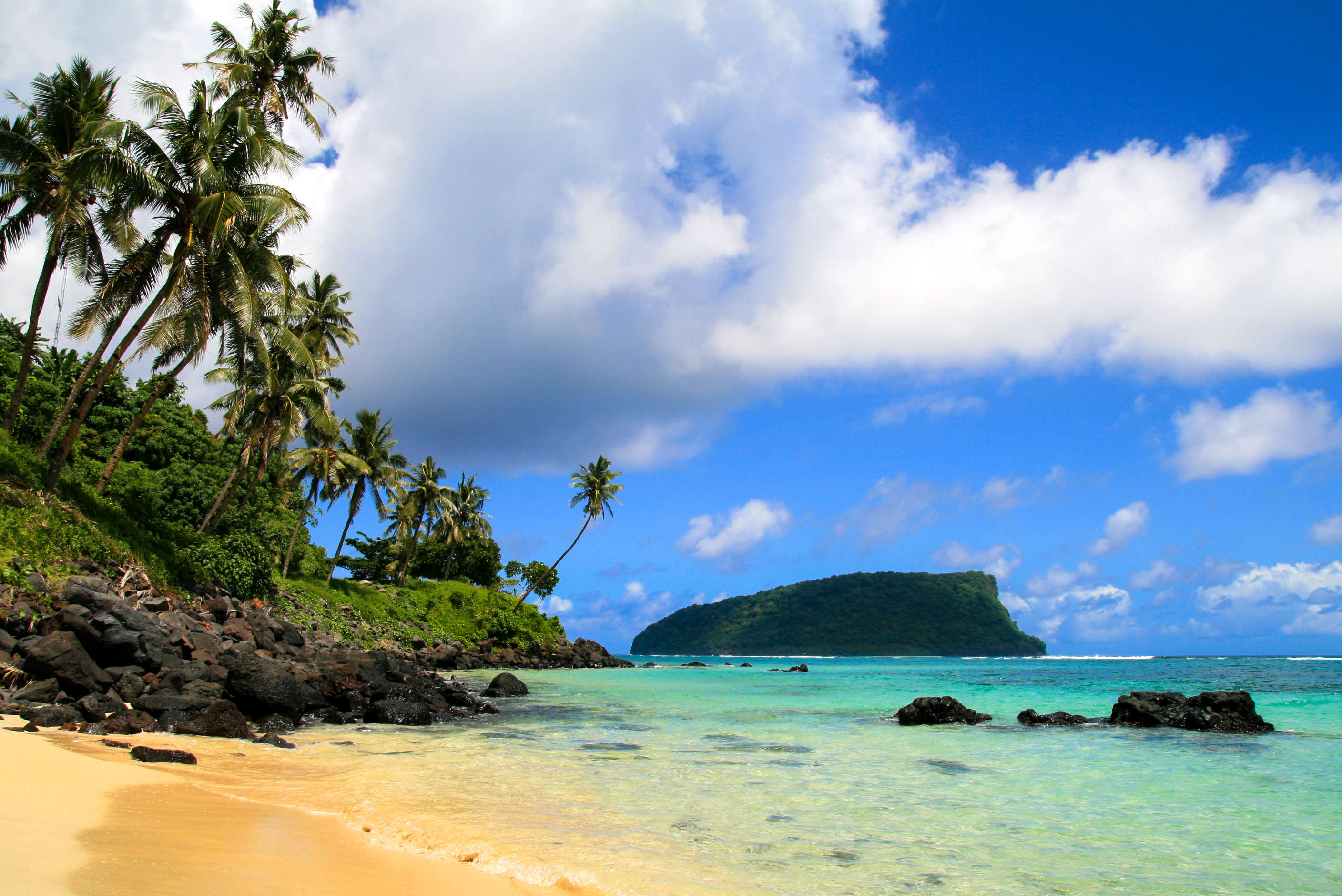 Tropical seascpape, golden sandy beach with palm trees and pristine blue waters of Pacific Ocean, view from Upolu to Nu'utele Island