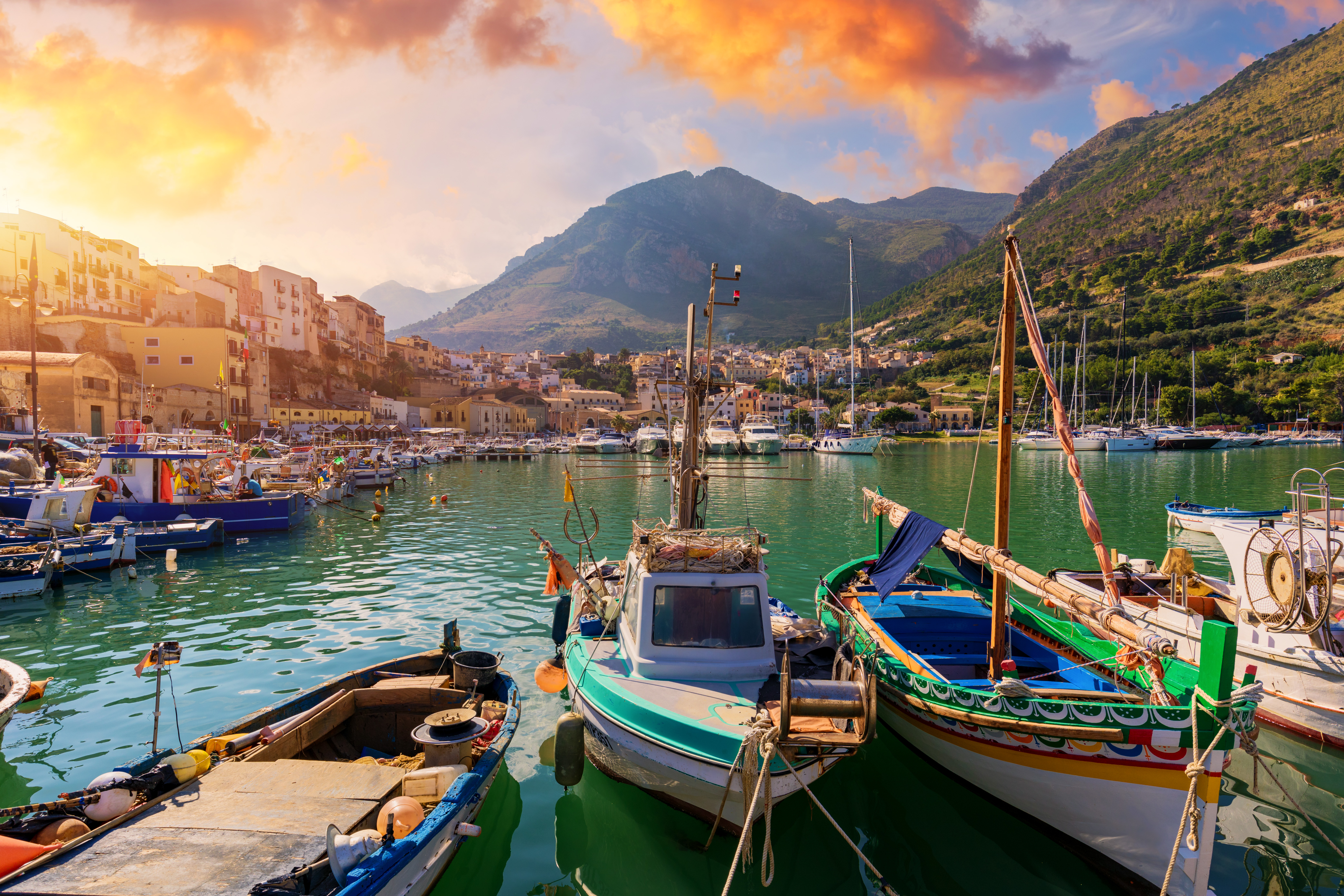 Fishing boats docked in the lovely seaside village with mountains and sun in the background
