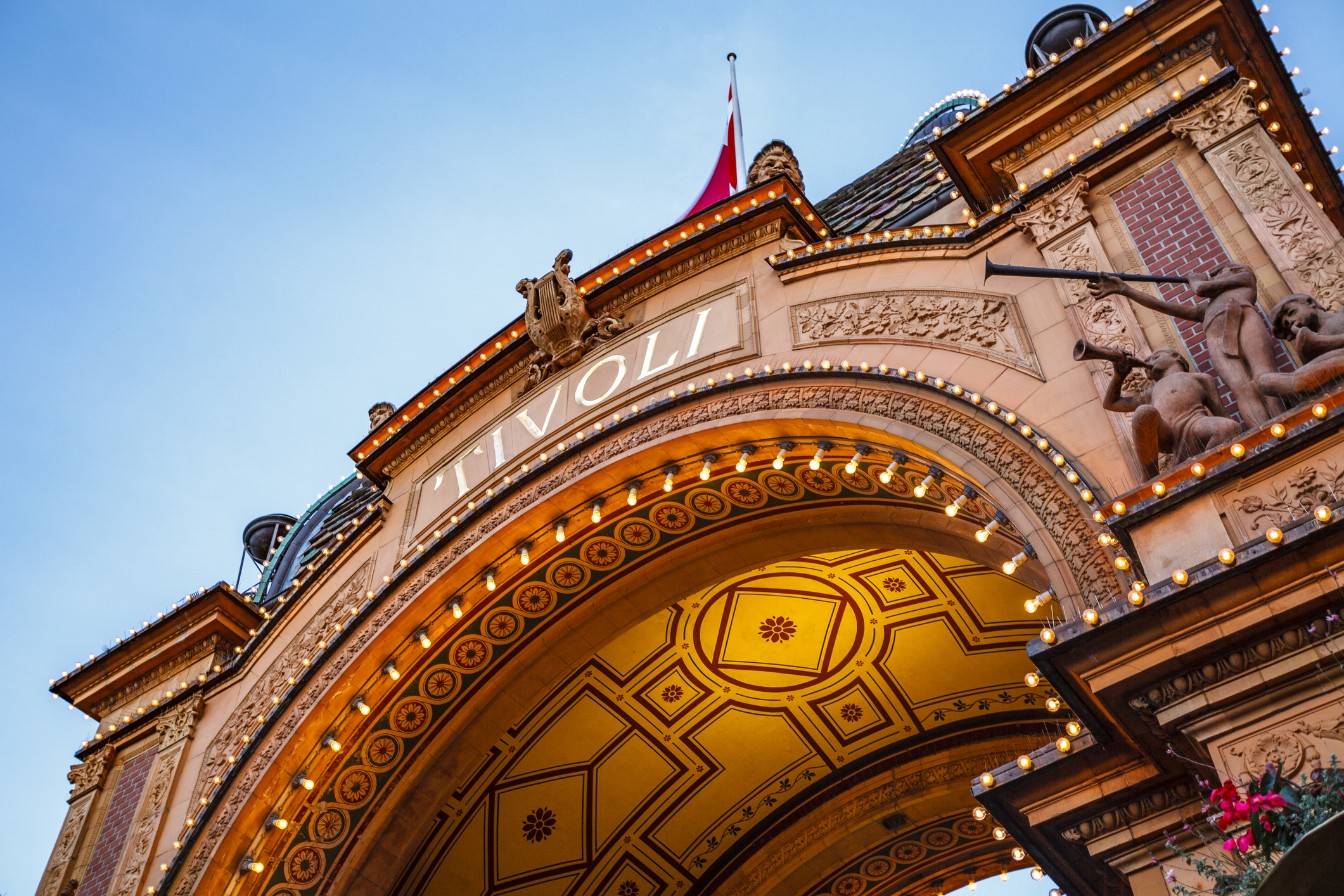 Archway of Tivoli Gardens, adorned with lights and decorative sculptures, against a clear sky.