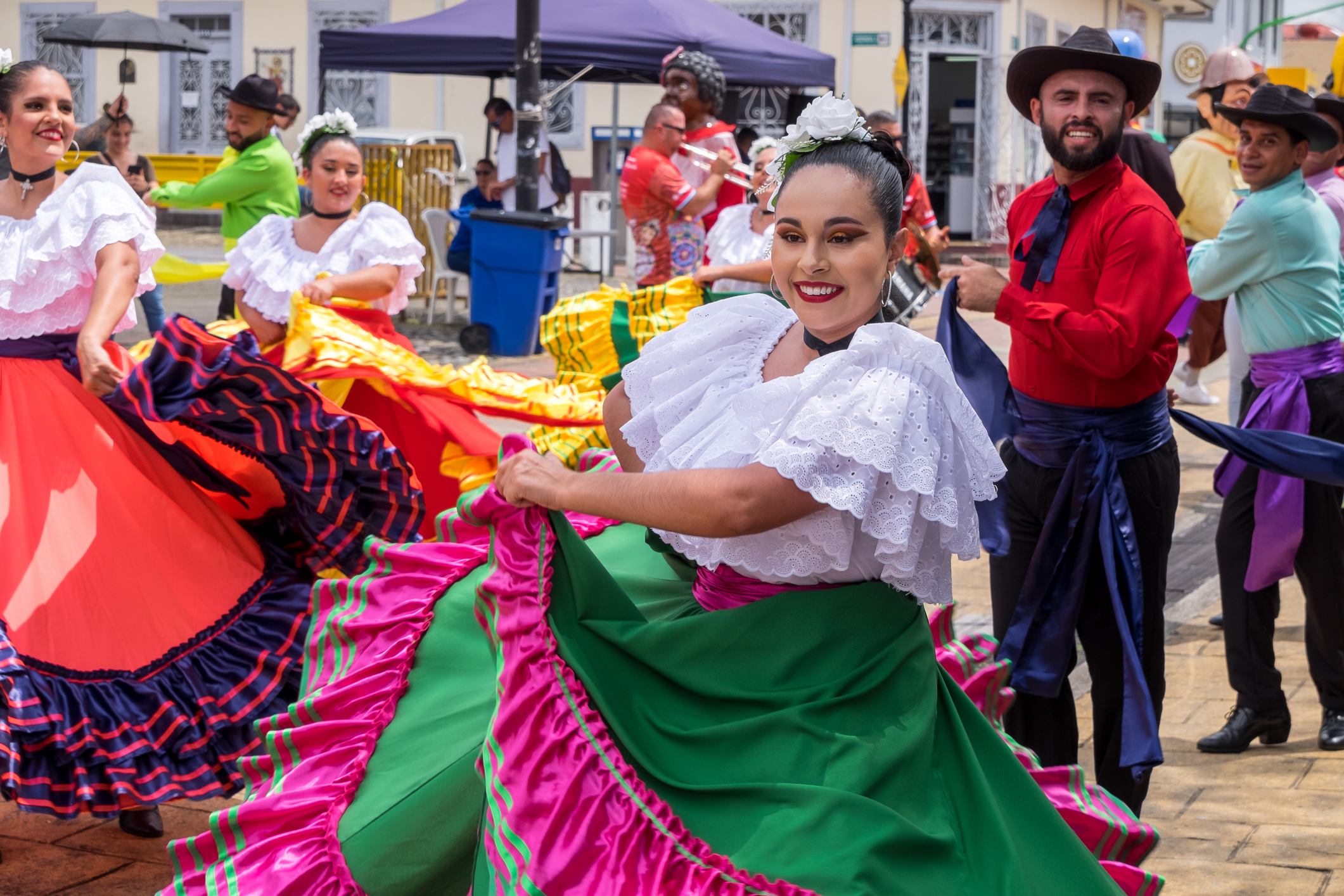 A group of dancers in colorful traditional costumes performs joyfully in an outdoor setting.